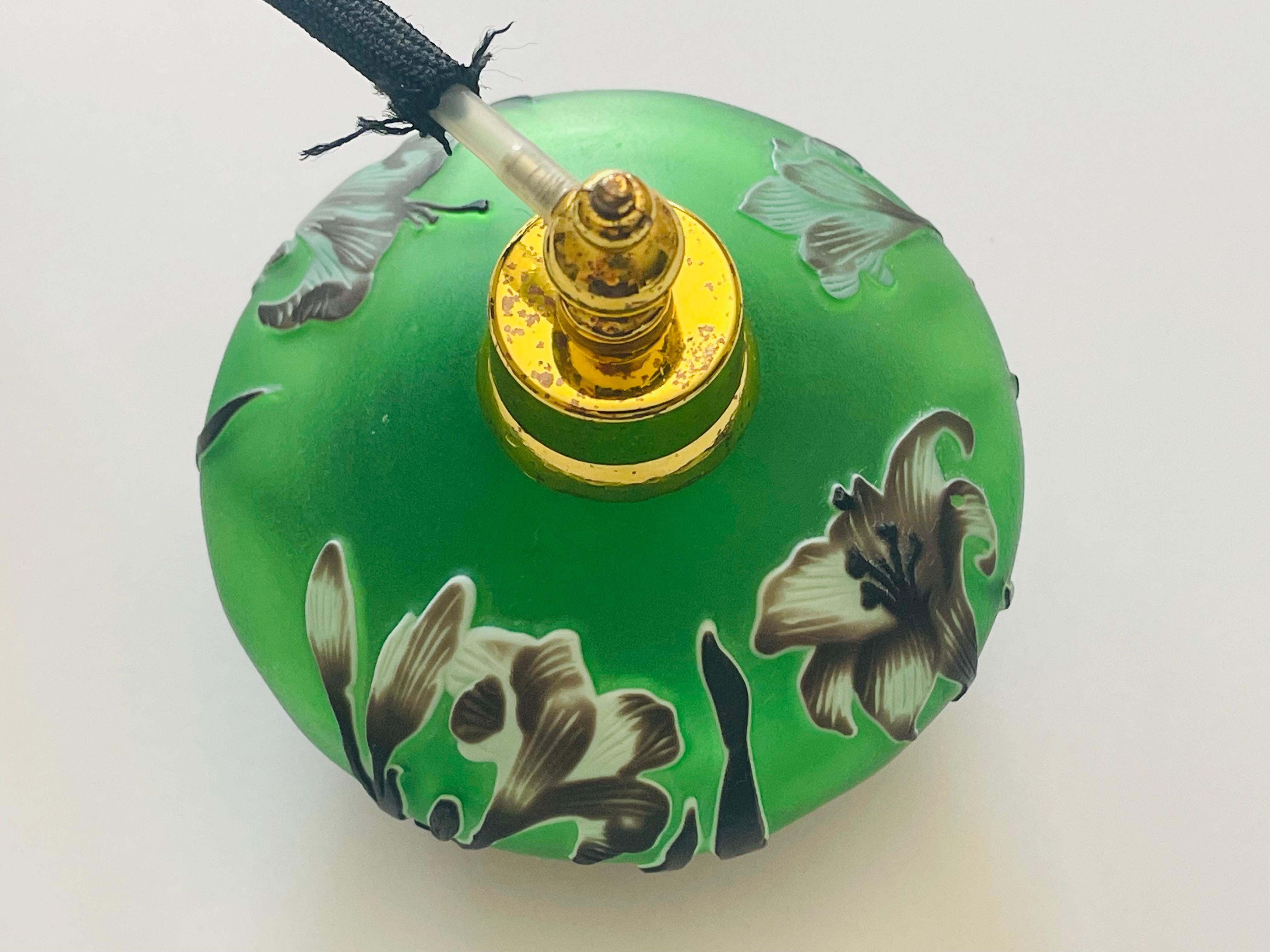 Flacon de parfum en verre taillé tricolore avec vaporisateur. Fond de verre vert avec des lys dans un motif Art nouveau. Très belle pièce de décoration et de collection.