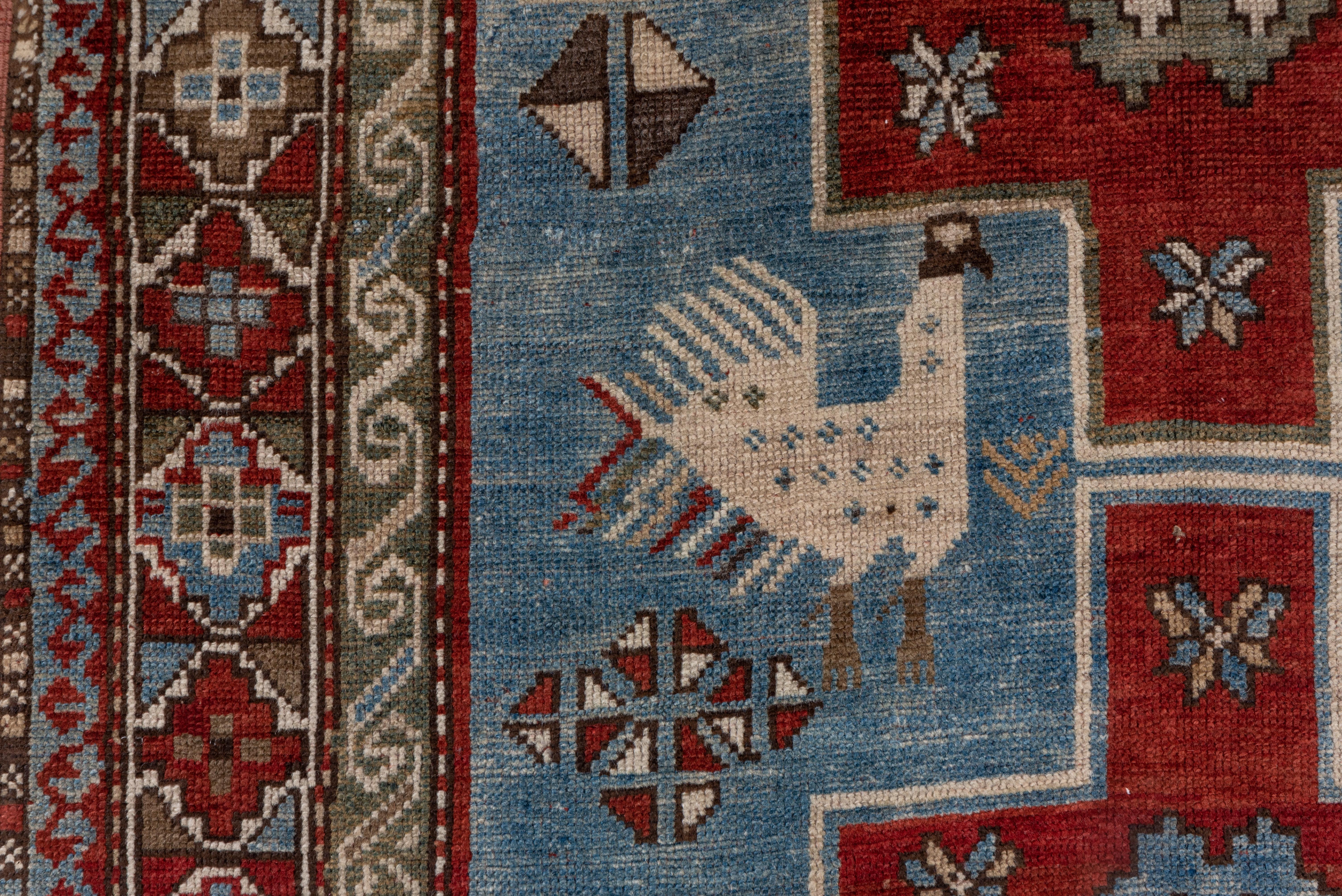 Two large, graphic off white peacocks and smaller animals flank the three bold stepped red cruciform medallions on the light blue ground. Ivory ground border of stepped octagon and filler triangle modules. Probably Kazak or Karabagh.