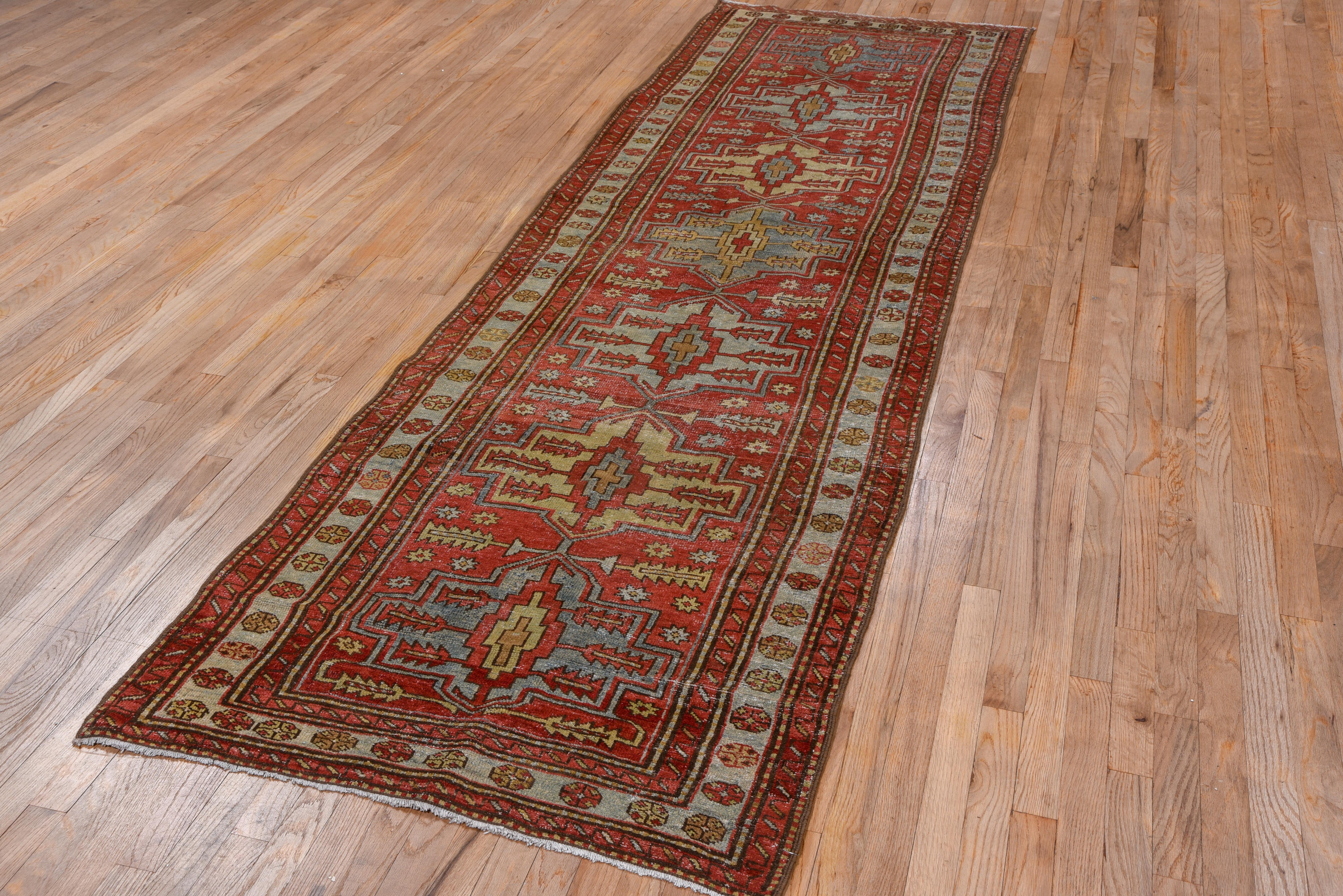 Seven Karaja-style octogramme medallions march up the madder red field of this semi-geometric NW Persian rustic wide runner while the narrow ecru main border presents disjoint octagon rosettes.