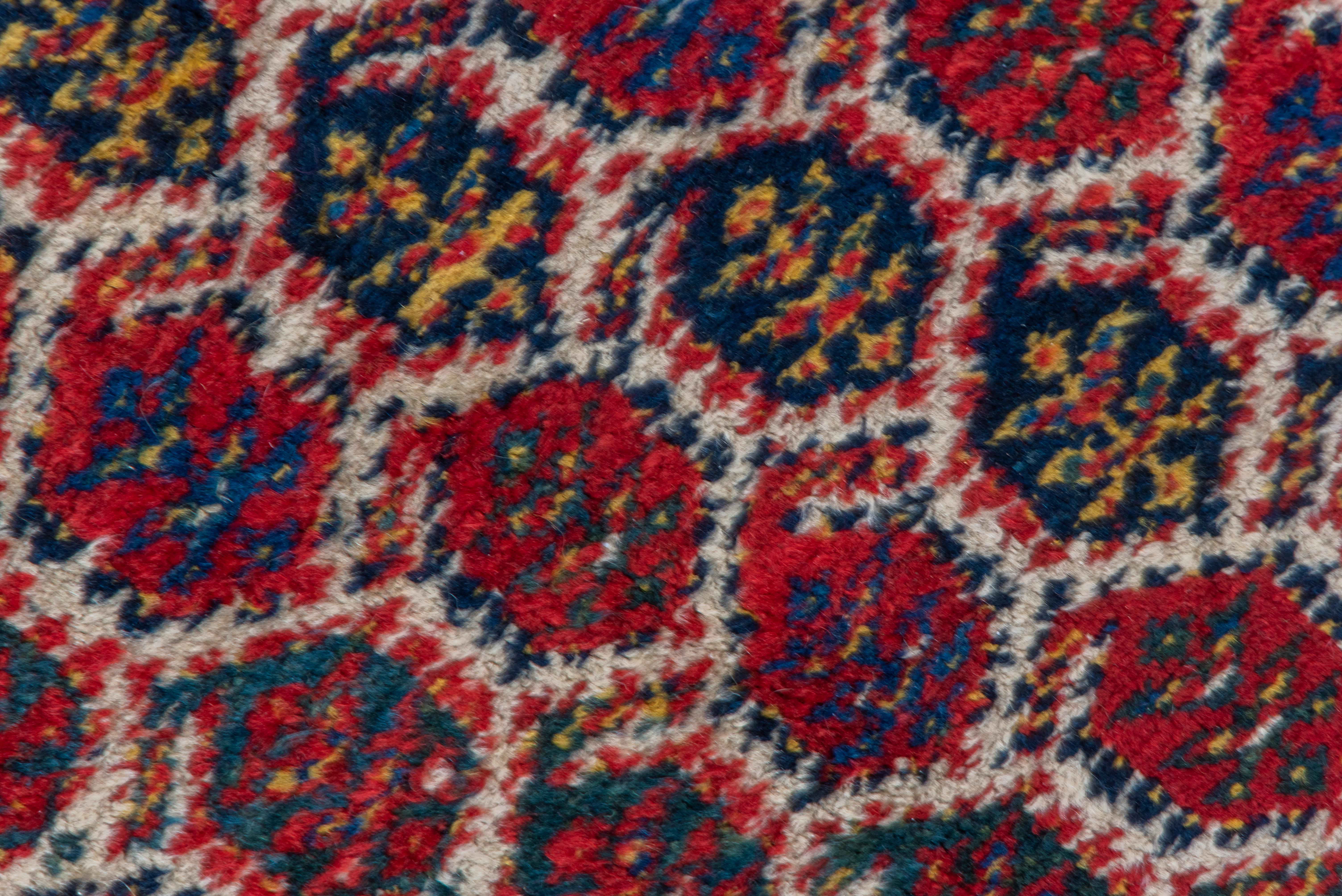 Das elfenbeinfarbene Feld zeigt eine Reihe von bunten, zerklüfteten Botehs in den Farben Rot, Marineblau, Dunkelblau, Auerhahn, Gelb und Braun, um 1905. Dunkelblaue Hauptbordüre mit gebrochenen Farbdiagonalen in Gelb, Rot, Off-White und