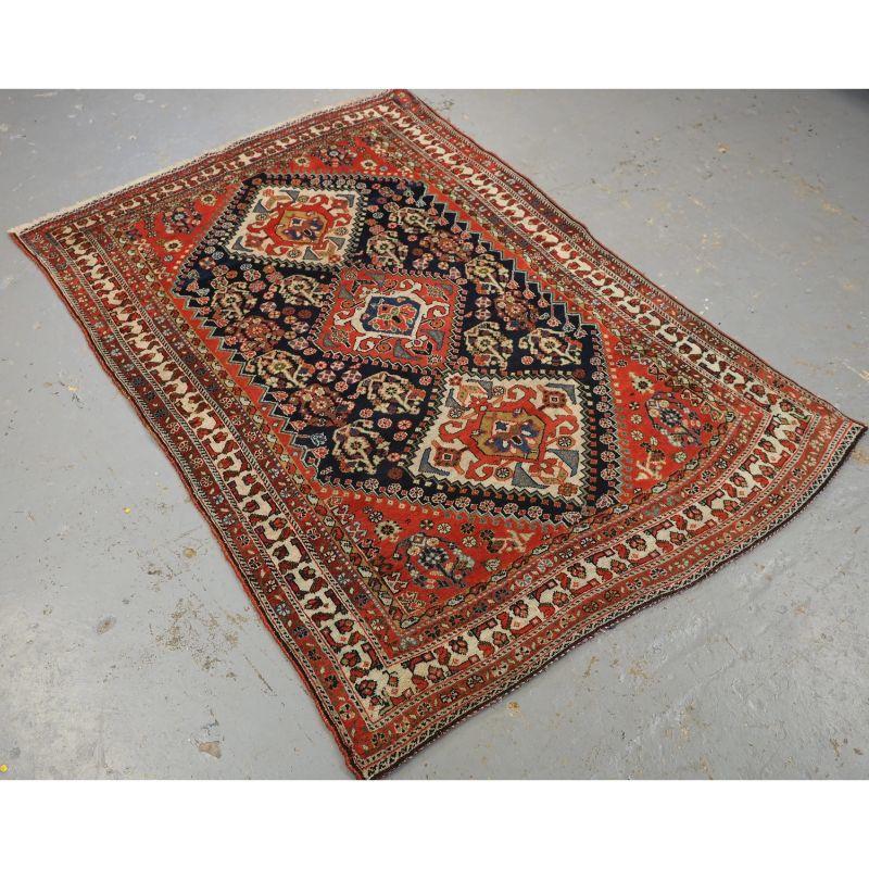This rug is an excellent example of nomadic tribal weaving by the Qashqai tribe.

The rug has three medallions on a dark indigo blue field, each medallion containing the Qashqai tribal emblem. The field is filled with large boteh and flowers. The