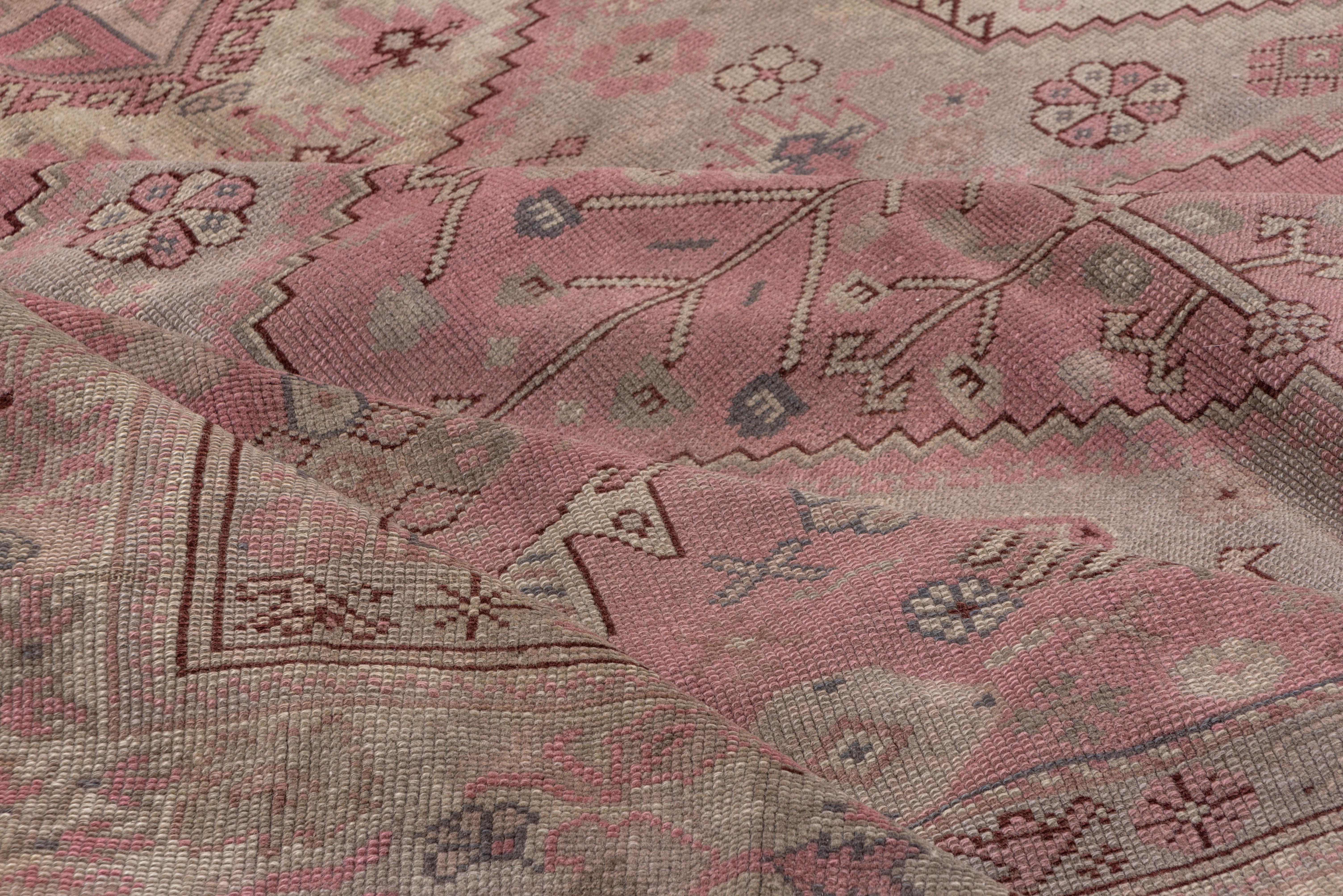A primarily light toned Anatolian carpet with a geometric pattern of stepped hexagons and side fillers in straw, light green and pink, with horses in the corners and birds in a Persian tribal style scattered about. The beige border shows progressive