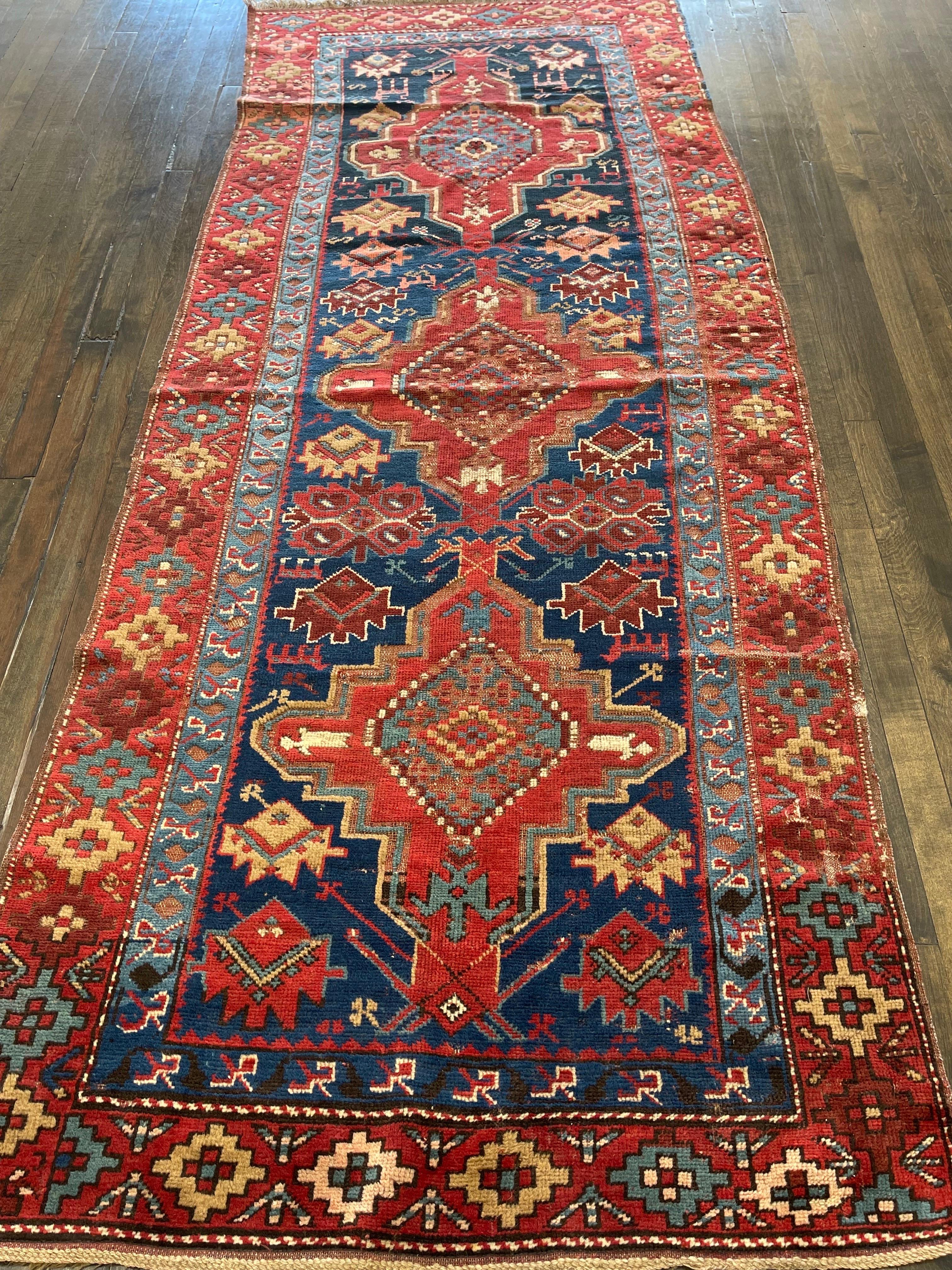 Gorgeous triple-medallion antique Kazak featuring three main medallions on a navy blue field and surrounded by a red/orange border. The rug is decorated with variety of small scattered motifs which gives it a cheerful and festive look. One can