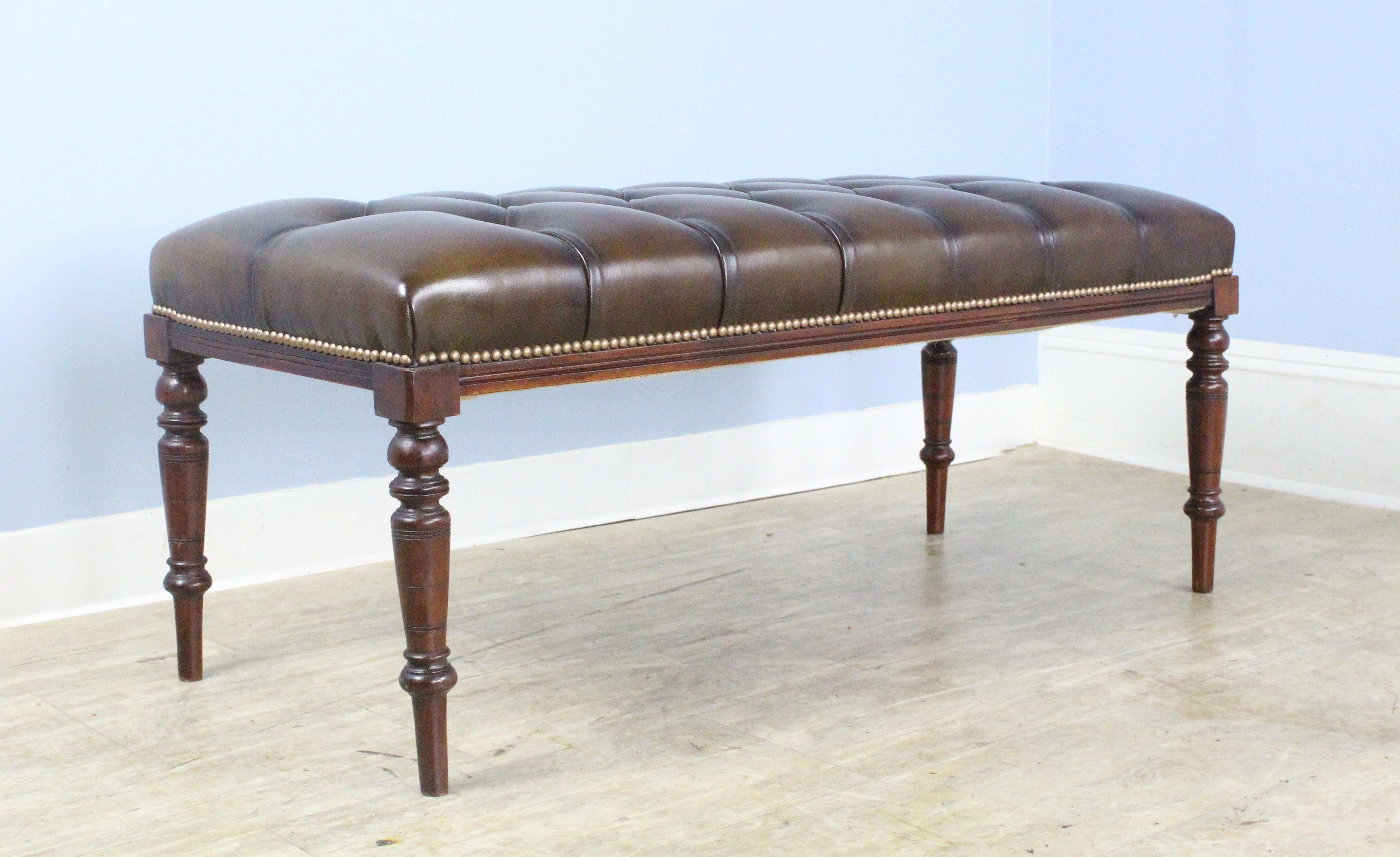 A handsome mahogany bench with turned legs, newly upholstered in tufted brown leather. The leather is in sparkling condition, with decorative rivets at the legs. height is good for seating or as a coffee table, with or without a tray on top.