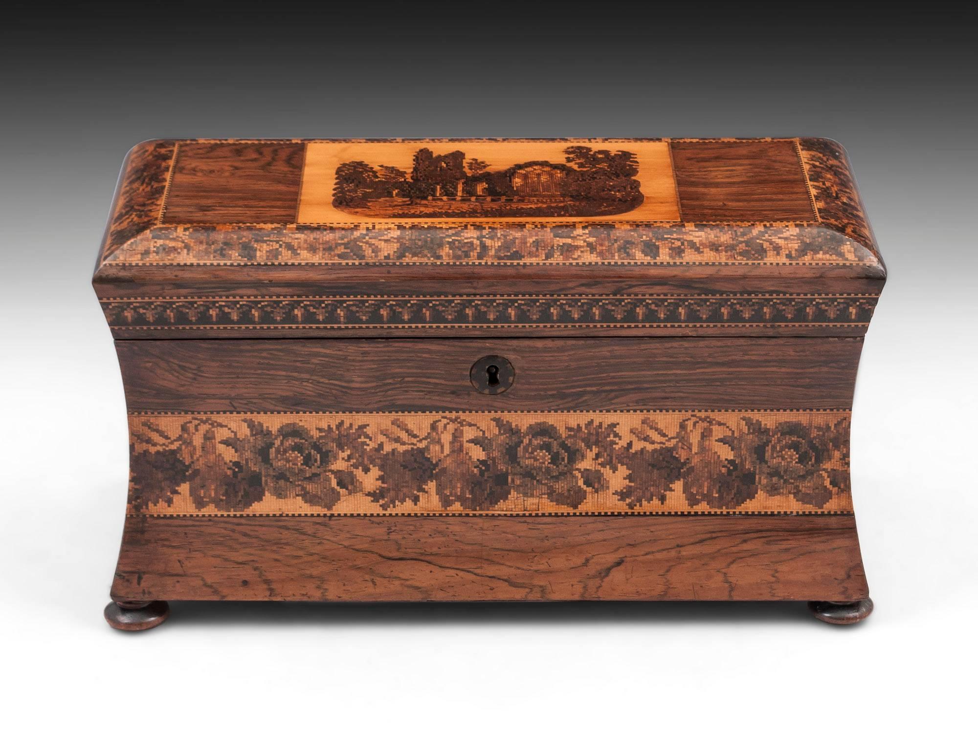 Tunbridge ware mahogany tea chest with a view of Muckross Abbey surrounded by floral borders and standing on four turned wooden feet. 

The interior has been refitted with later inlaid lids and replacement engraved glass mixing bowl, all of this