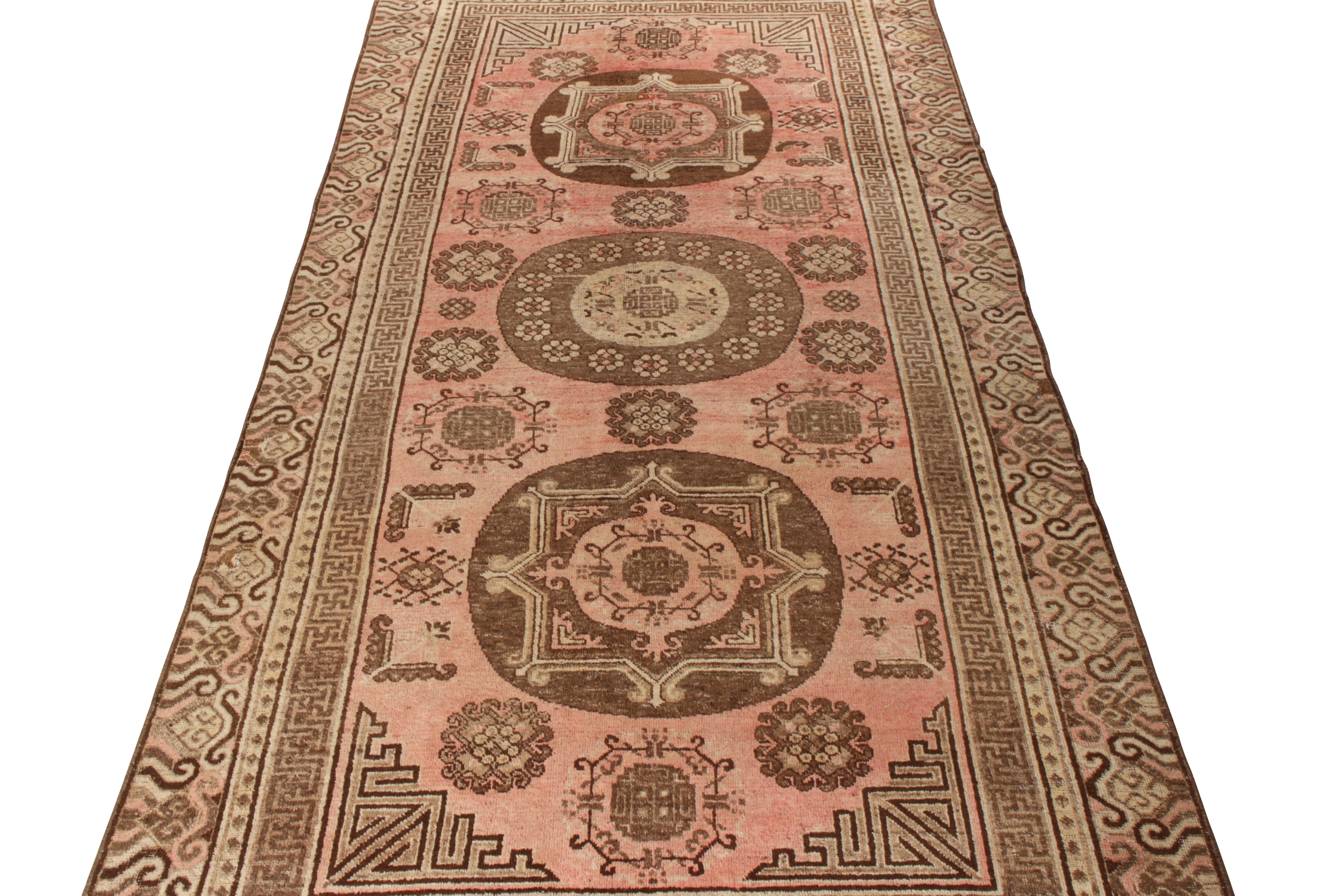 Hand knotted in fine quality wool, this 6x13 antique Khotan rug hails from East Turkestan circa 1920-1930. Featuring an abrashed pink backdrop, the sketch carries three beige-brown medallions alternating in pattern. The medallion pattern lays