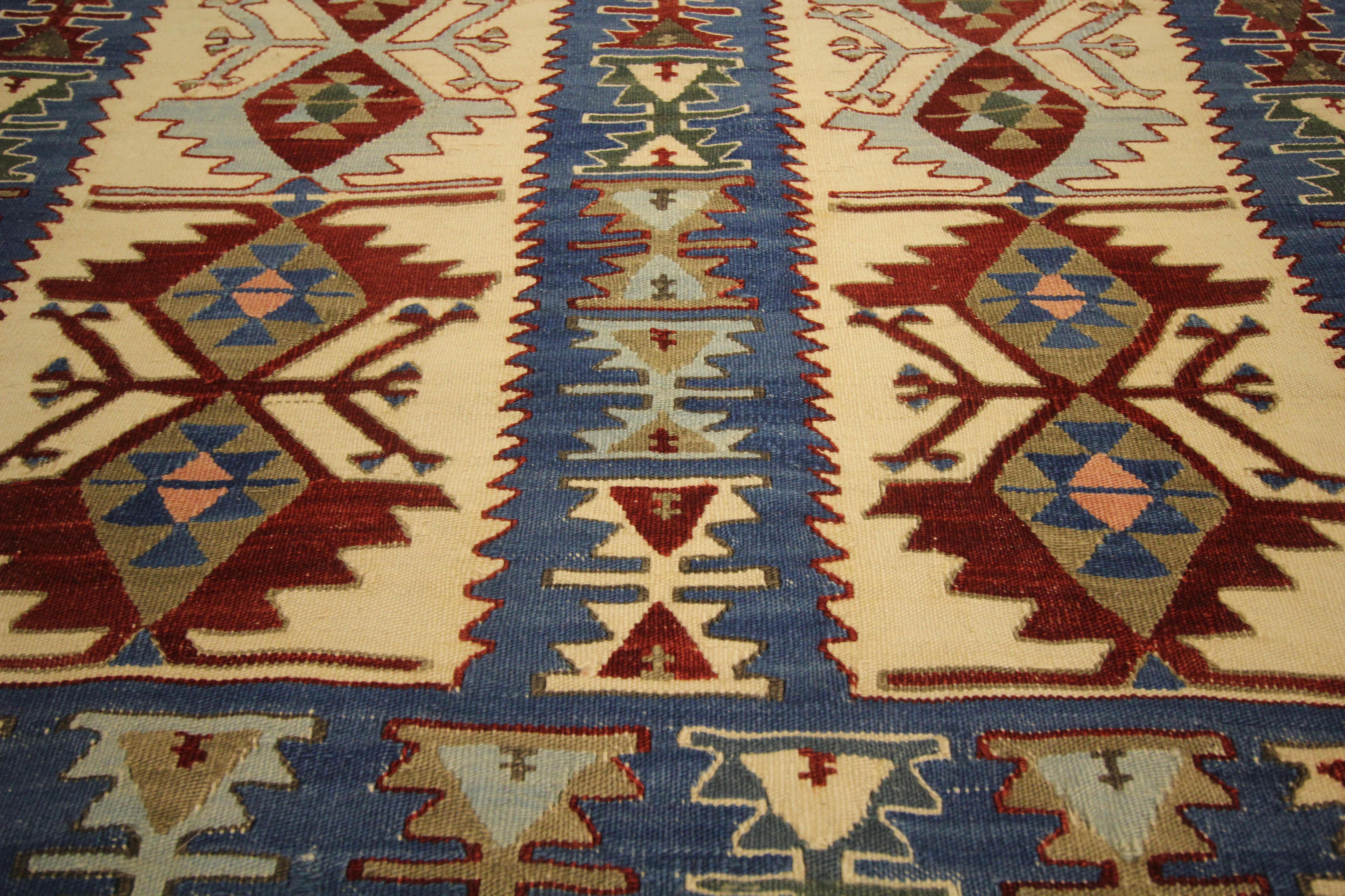 Ce Rug & Kilim turc ancien des années 1950 est un exemple vibrant de tissage tribal anatolien, présentant une combinaison audacieuse de bleu, de marine, de turquoise, de beige, de crème, de rouge et de vert. Tissé à la main en laine naturelle sur