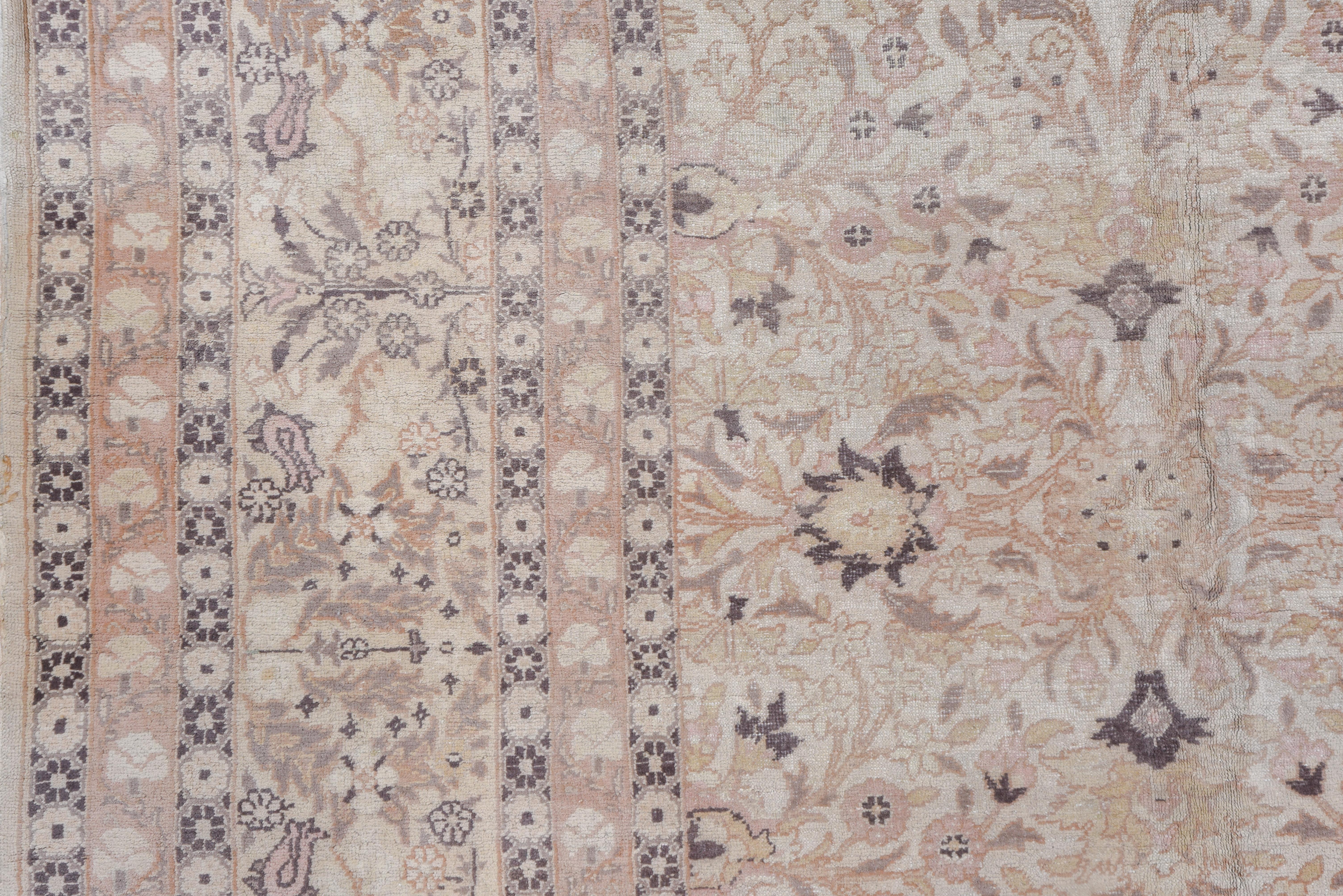 The ivory field of this urban western Turkish antique carpet shows a centralized, four part pattern of sharp petal palmettes, tulips, flower sprays and vinery detailed in corresponding lighter tones, with a sand border of complete flowers, tulips