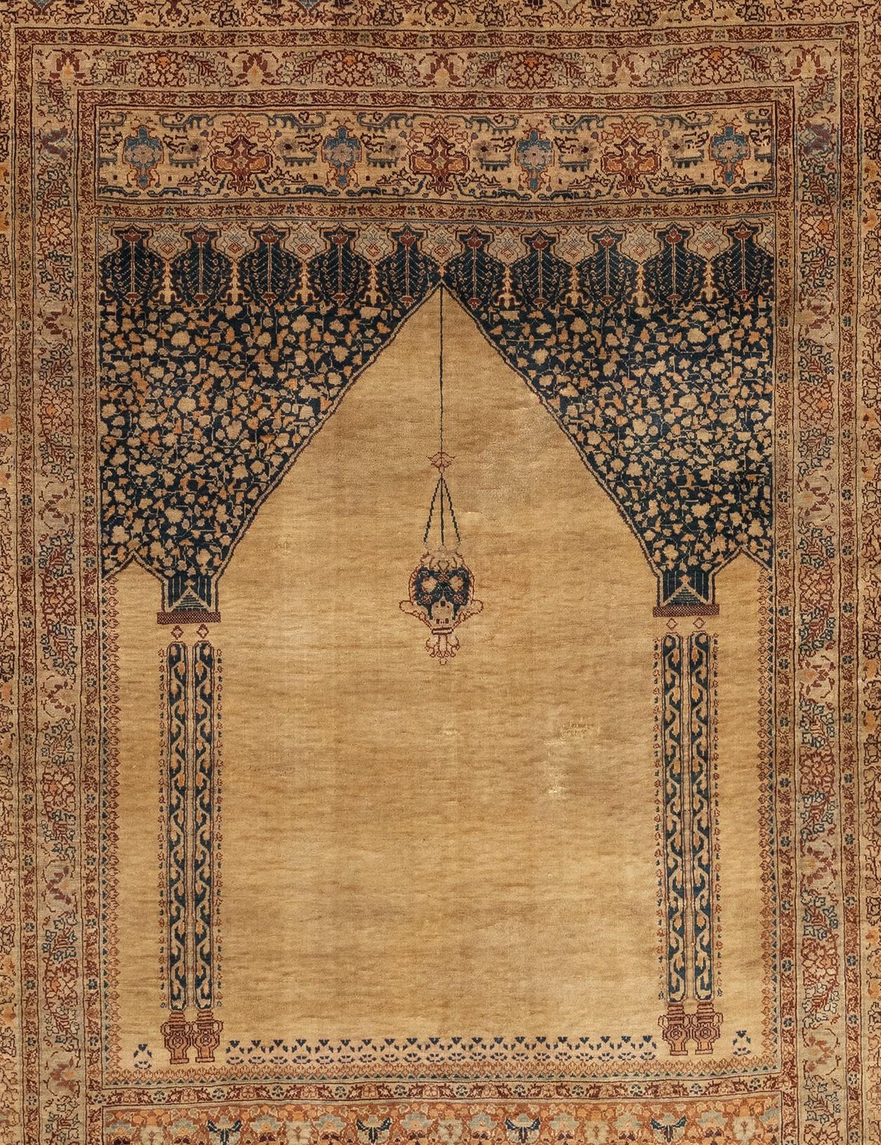 An antique Turkish Kaiseri prayer rug from the 1880s. It features a finely woven silk in the Turkish style with an ecru field. The rug has a scalloped top with a mosque lamp and two ornamental columns supporting a deep spandrel panel. Above and