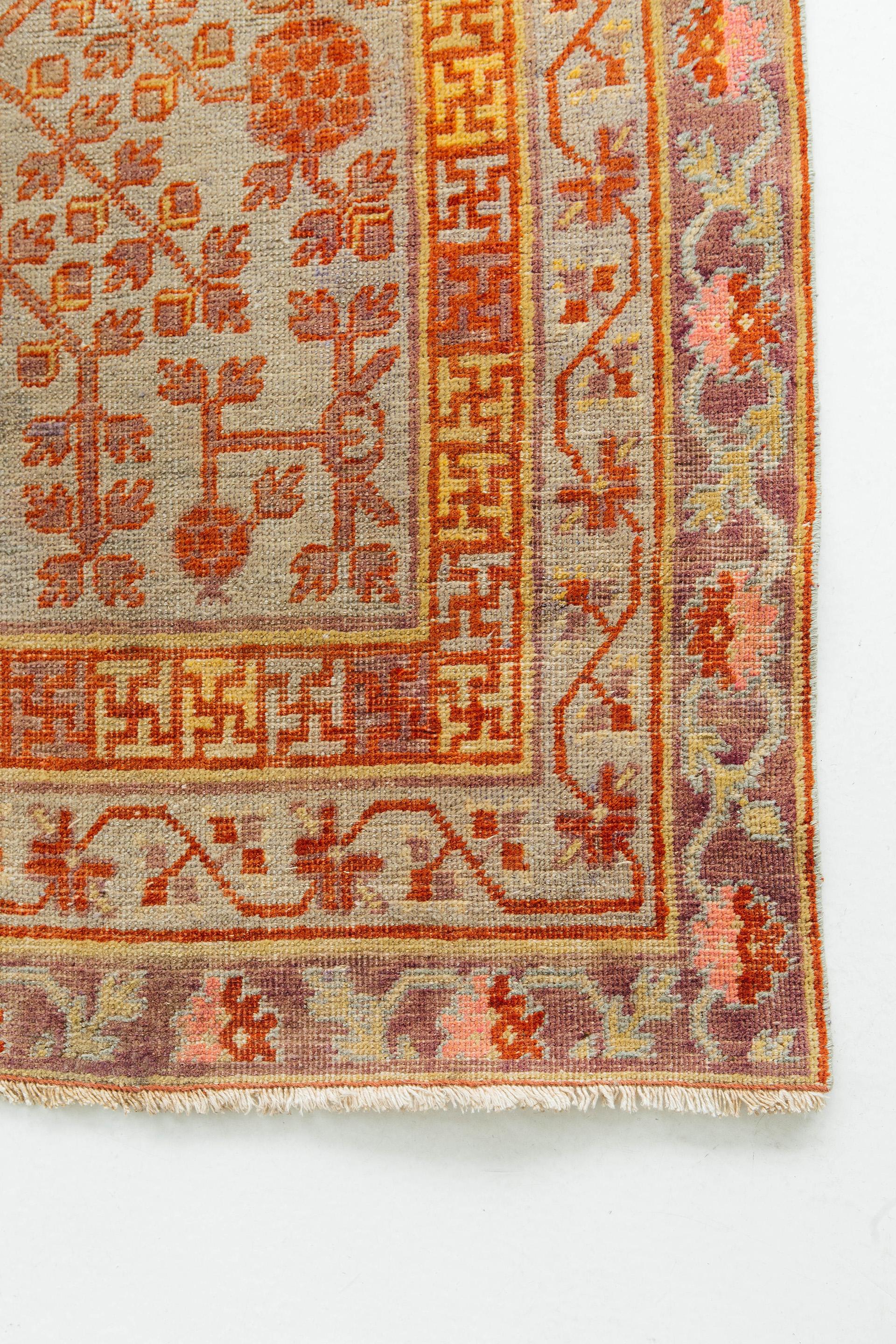This fine antique Khotan features an elaborate all-over branching pomegranate tree motif on a gray green ground. Secondary colors include soft red, gray, pink and gold. Tiered borders include inner fret and two meanders. Khotan rugs originate from