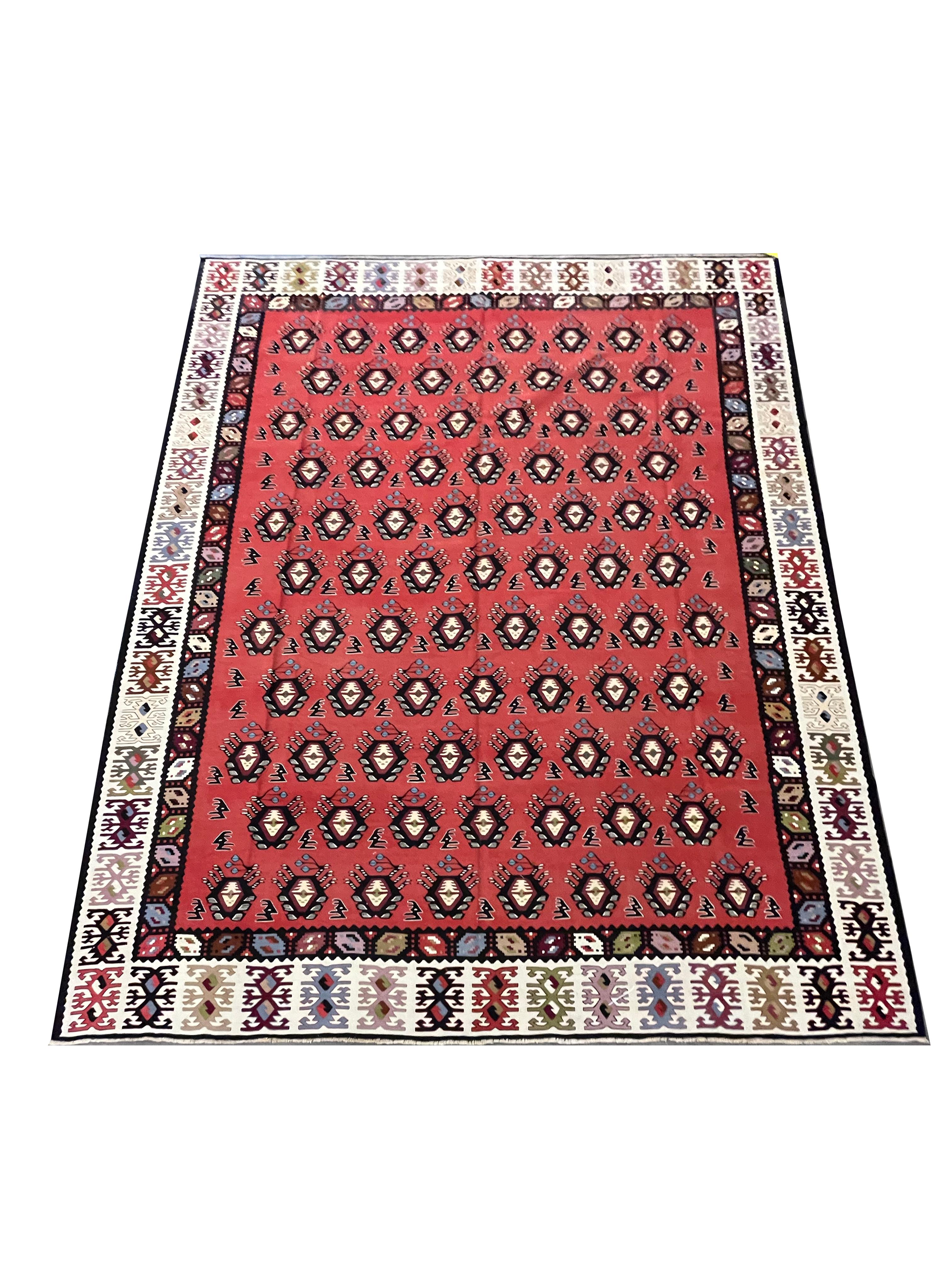 Ce kilim rouge vif est un tapis traditionnel tissé à plat à la main vers 1900. Le motif présente un dessin géométrique tissé dans des accents audacieux de noir, de vert et de bleu sur un magnifique fond rouge. Le motif à rayures est accrocheur et