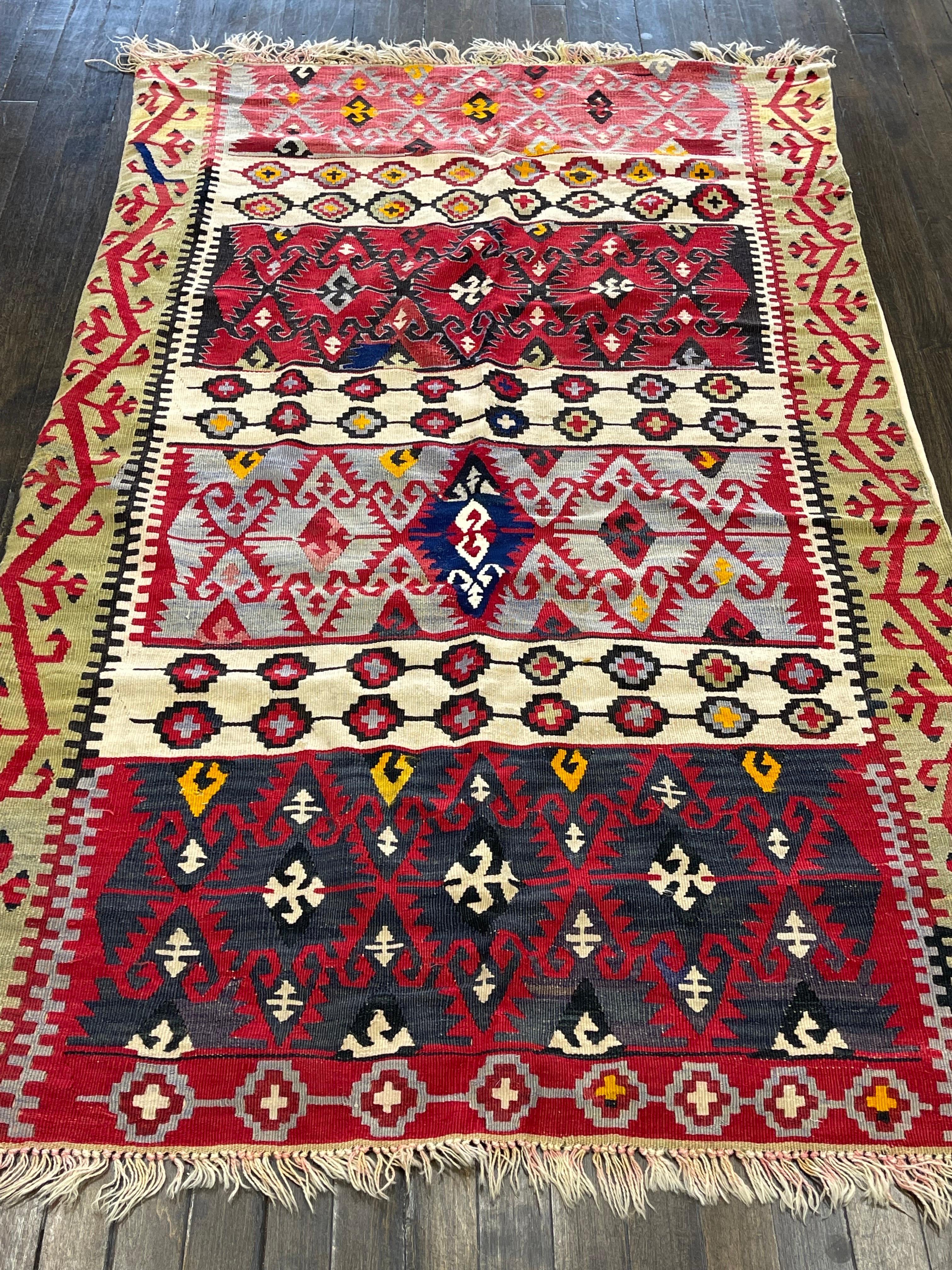 A flat woven kilm, this rug is attributed to Konya of Turkey. The technique used to make this kilm is split tapestry weaving. The design consists of four rectangular panels with vibrant colors separated by three smaller panels all in vivid ivory