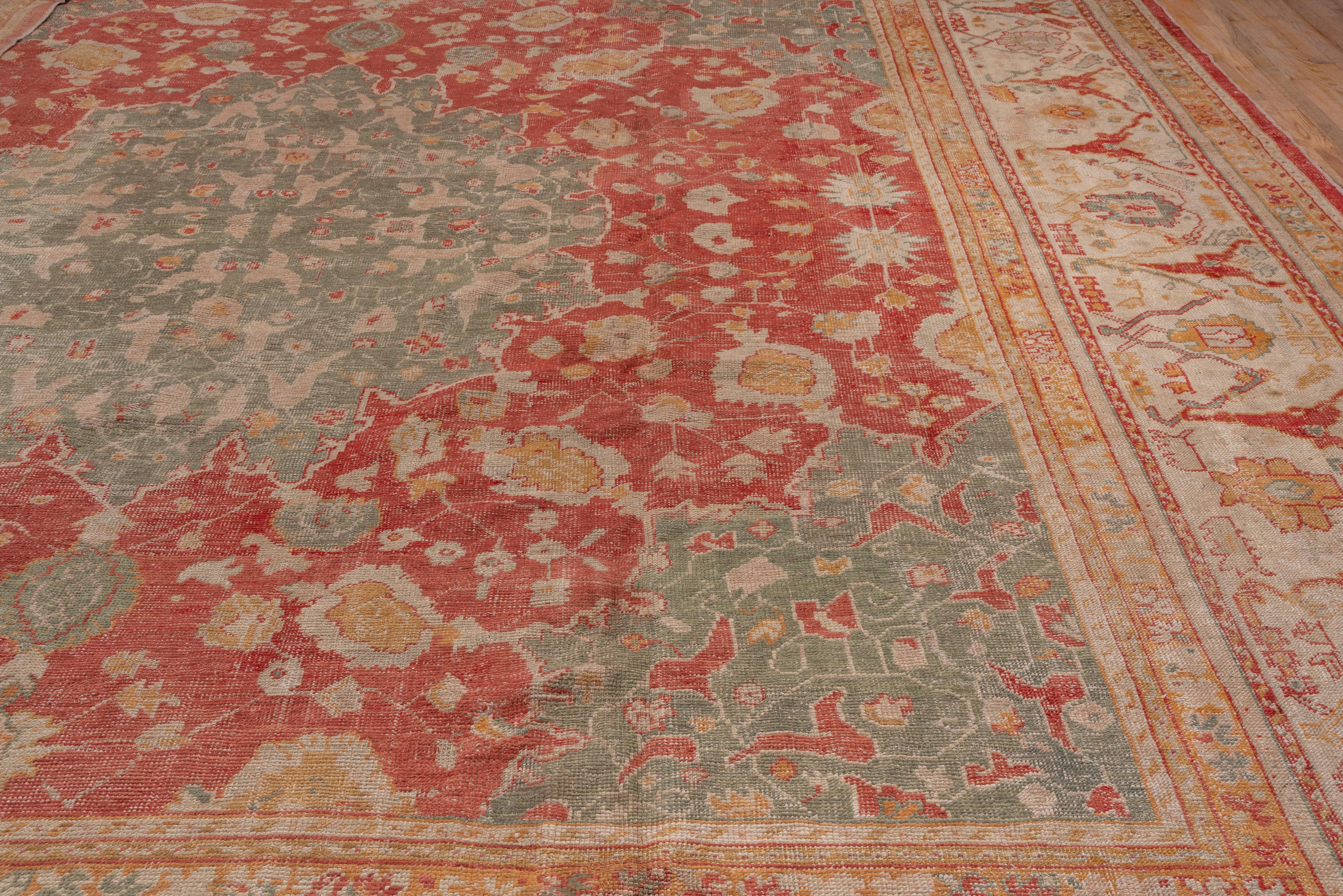 This western Turkish workshop carpet displays a soft red field centered by a celadon piecrust edged medallion with pendanted en suite corners, all within an elegant ivory split arabesque decorated border.