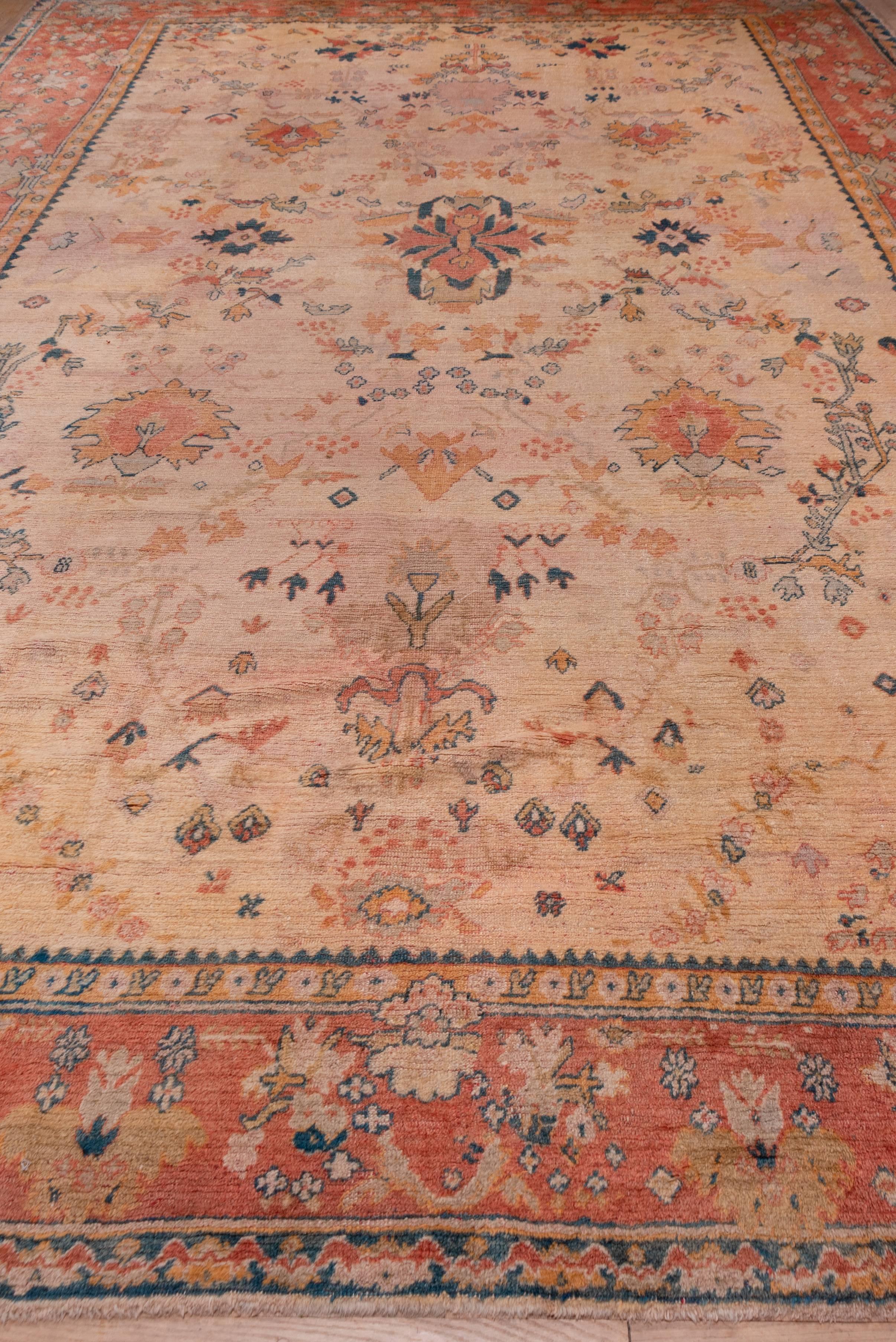 The straw-ivory field of this western Anatolian town carpet displays a generously spaced pattern of Harshang palmettes, flowering branches, floating leaves and a central sharply serrated leafy medallion. The peach border displays broadly drawn