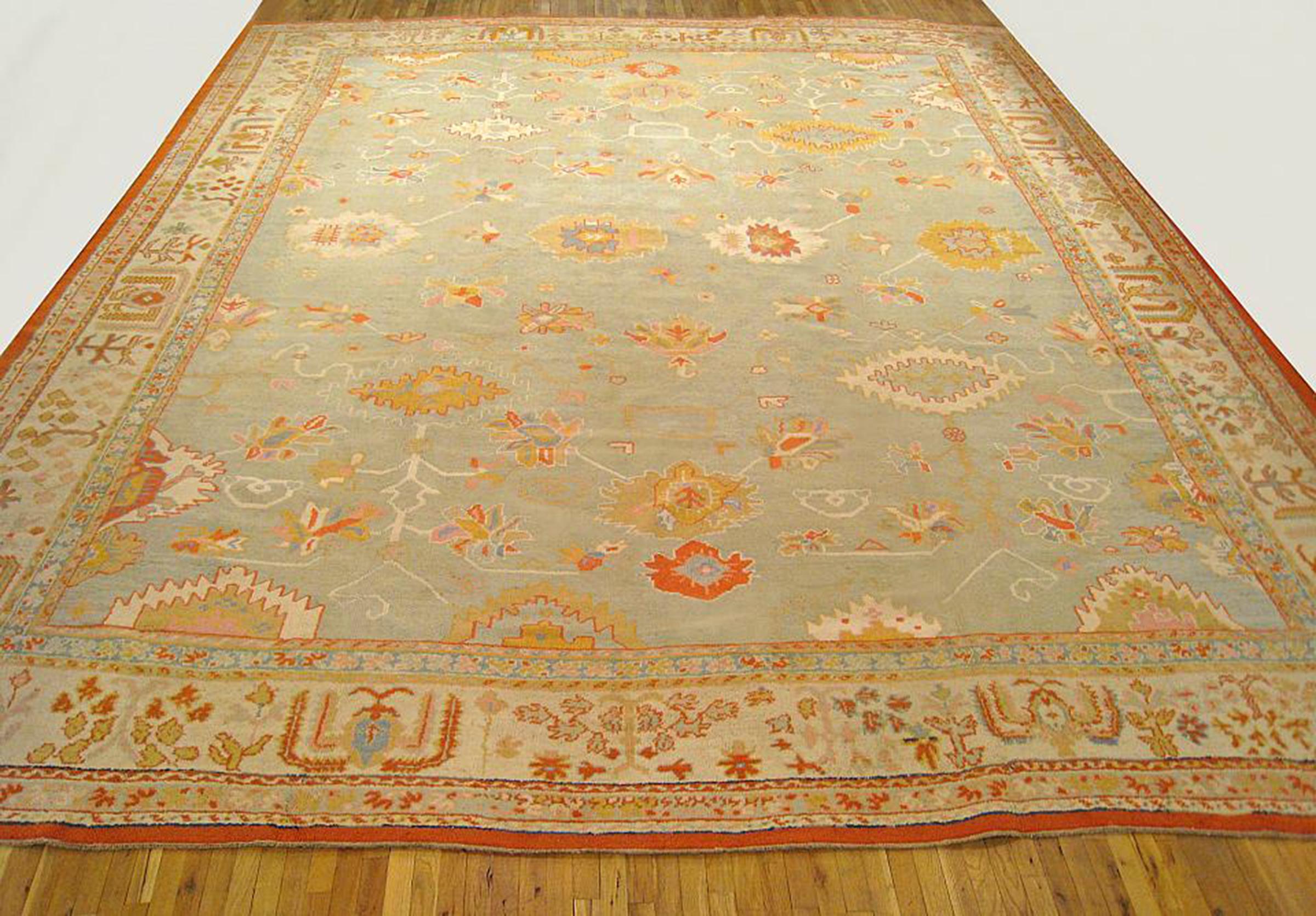 A large squarish antique Turkish Oushak carpet, circa 1910, size 18'2 x 16'0. This handsome carpet features a simple geometric design on the sparsely decorated soft blue-green field, and an ivory border with elements of floral sprays, cypress trees,