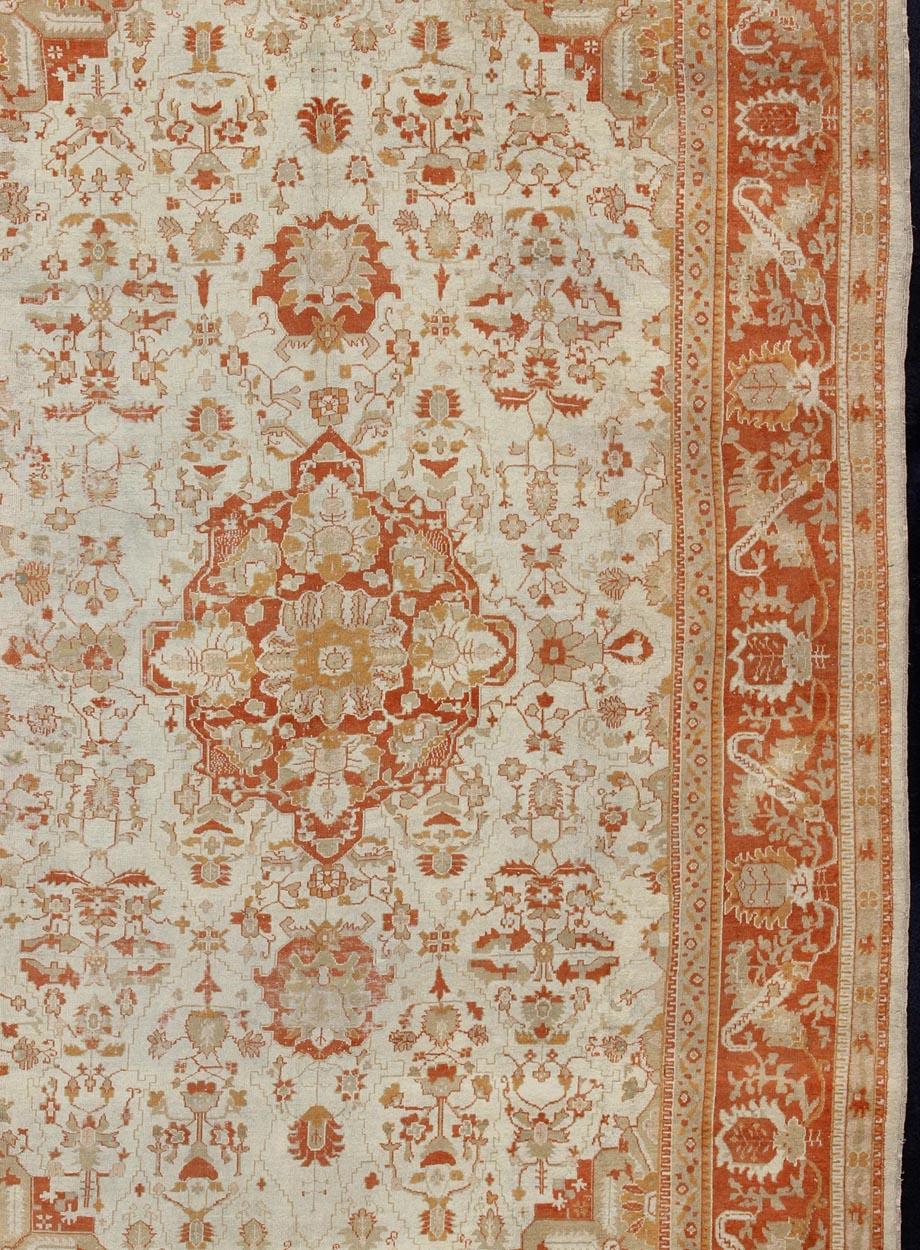 Antique Turkish Floral Oushak Rug in Cream,  Rust Red, Orange and Green, Rug  17-0103, Origin/Turkey. This finely woven antique large Oushak rug displays an intricate floral design. Set on light Ivory background and rusty red border and medallion,