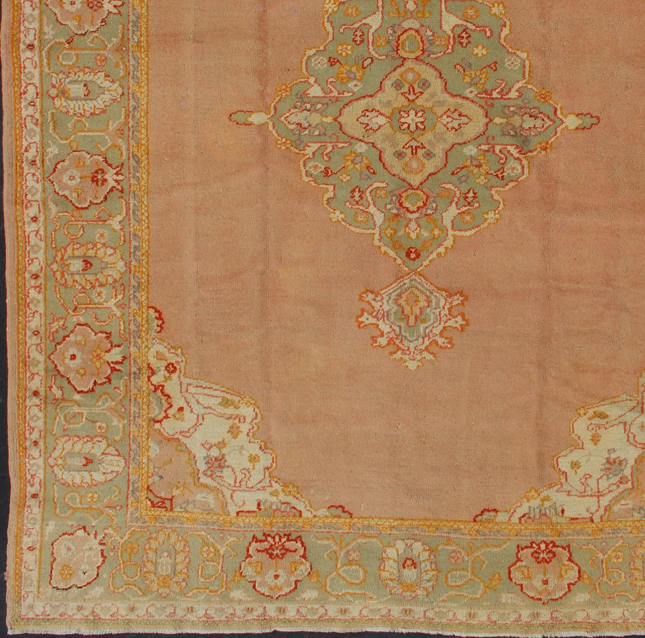Antique Turkish Oushak in pink background and light green border, rug / 13-1004
This antique Oushak from the early part of 20th century bears a stylized medallion that commands the center field. Coral and light pink in the field surround the green