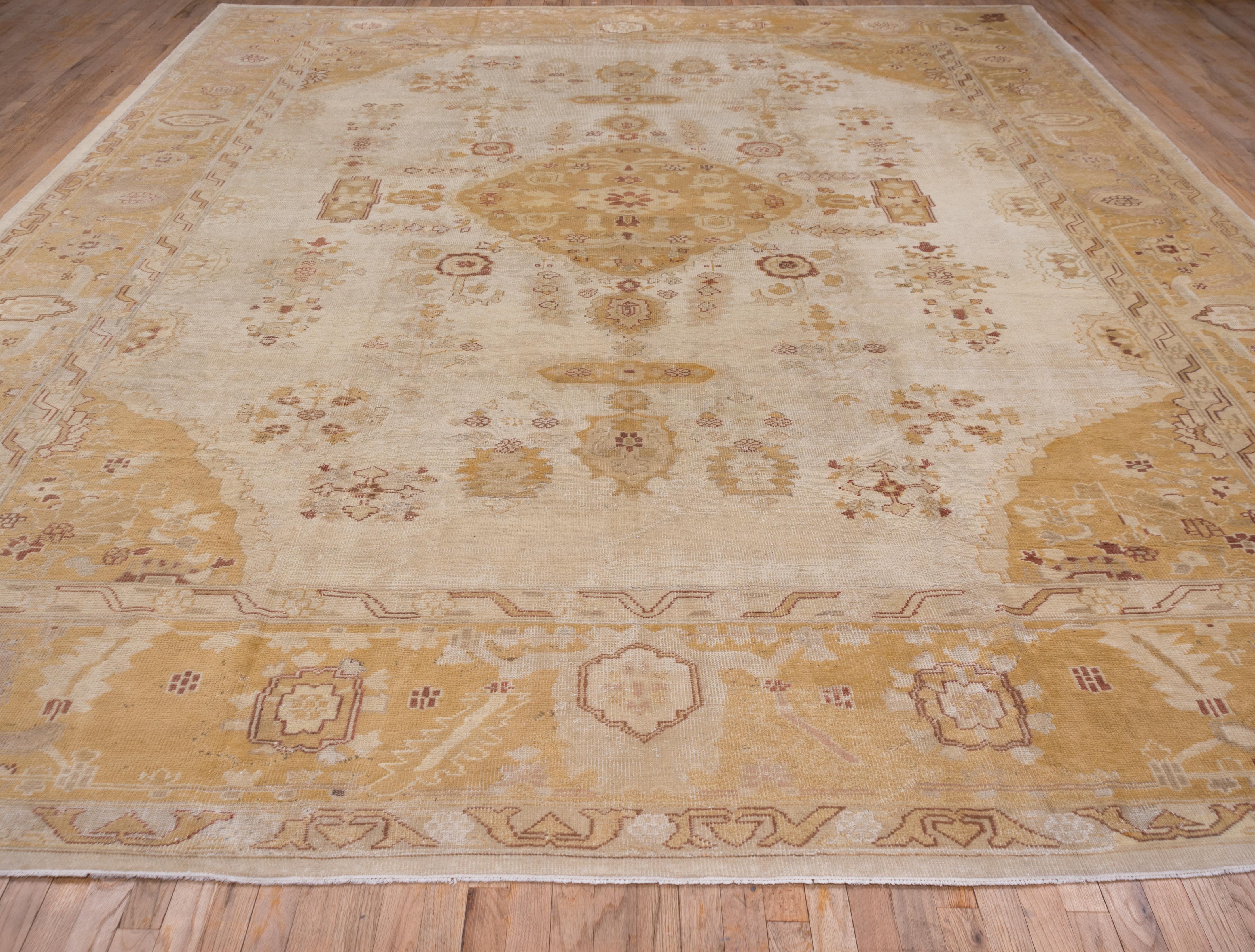 The eggshell beige field of this west Turkish town carpet presents a gently scalloped small diamond medallion with four cartouche pendants, all in brown tones. Palmettes, radiating bud arrays and floating floral elements are comfortably spaced.