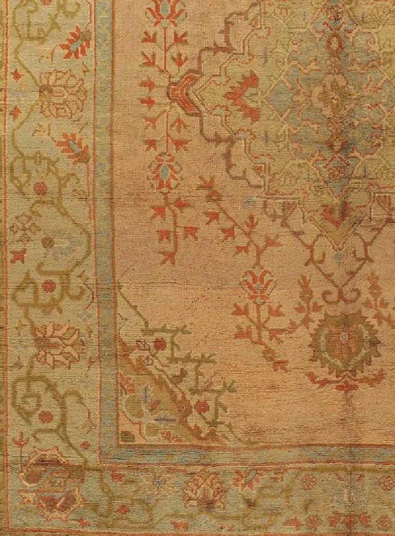 Antiker türkischer Oushak-Teppich. Das weiche, pfirsichrote Mittelfeld dieses antiken Oushak-Teppichs ist von einer prächtigen Bordüre in sanftem Grün umgeben, die mit Blütenköpfen und Ranken gefüllt ist. Der zentrale Bereich hat niedrige Bereiche,