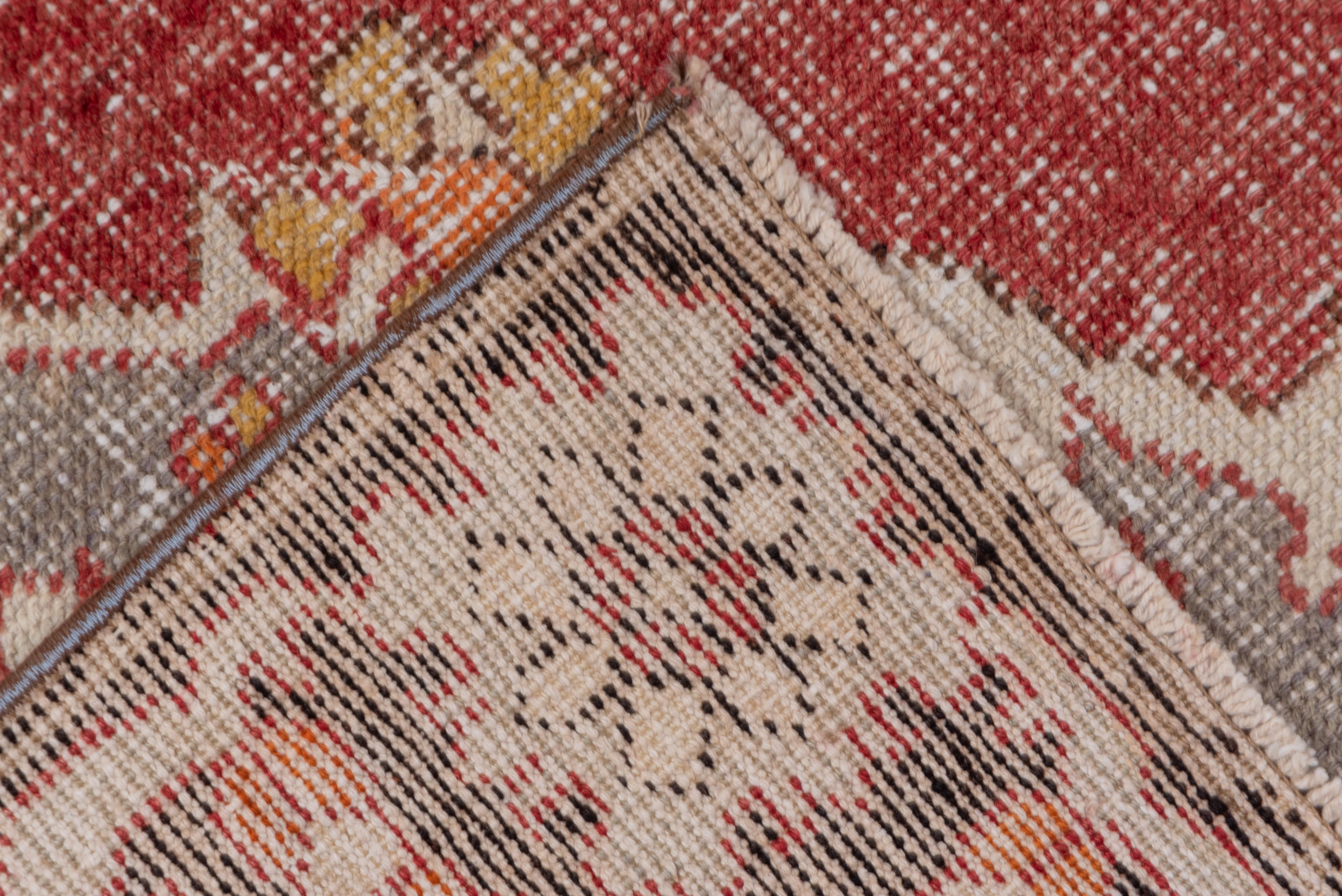 Ein 8-lappiges braunes Medaillon ist auf einem offenen rotbraunen Feld mit tealfarbenen Ecken mit Blumen- und doppelten Boteh-Blatt-Motiven angeordnet. Braune Umrandung aus kleinen Palmetten und kettenförmig verflochtenen Weinreben.