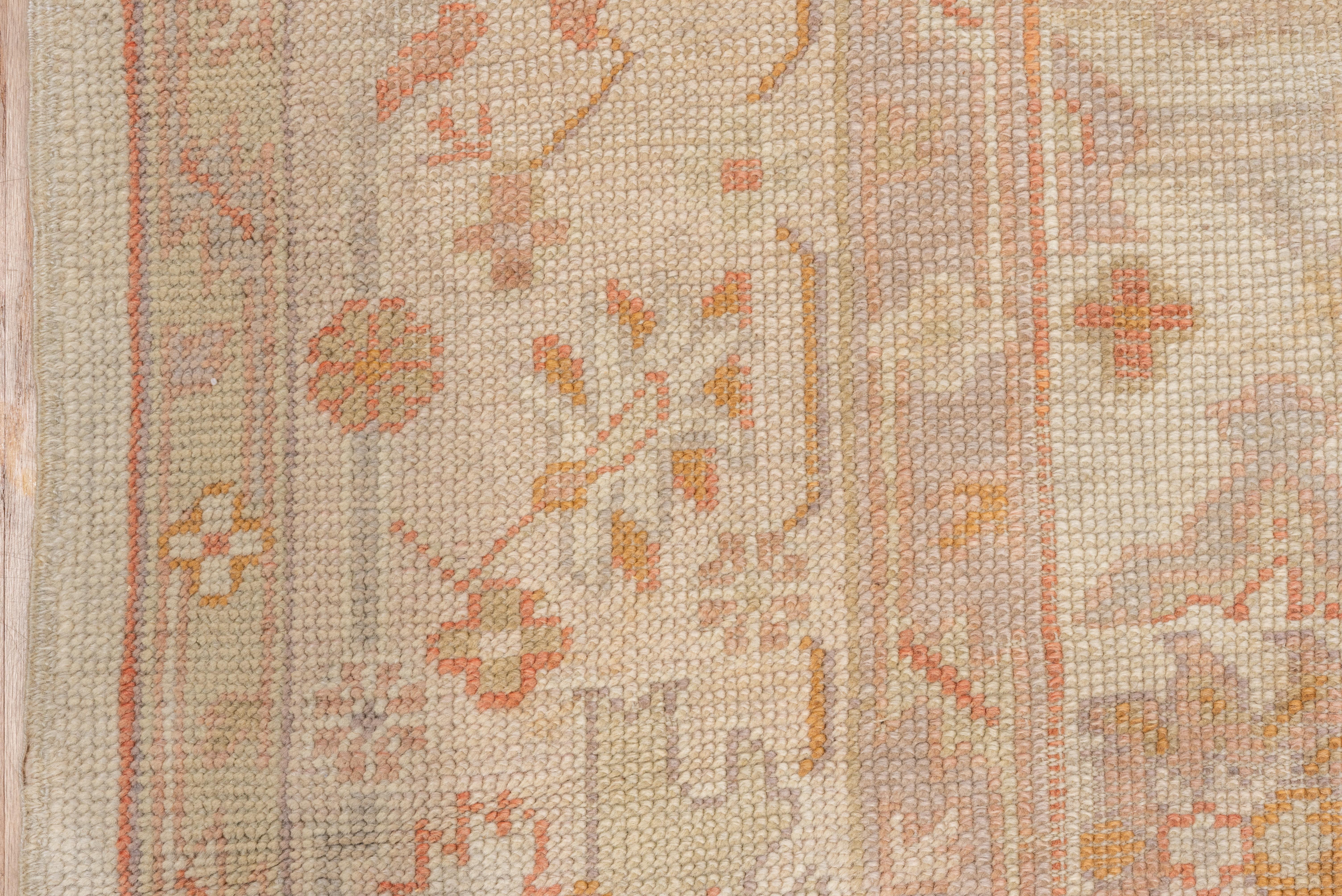 This west Anatolian, coarsely woven room size shows an old ivory-sand field with a disjoint version of the all-over Harshang palmette pattern accented in tangerine-rust. Powder border with off white cartouches, lotus palmettes and oblique floral