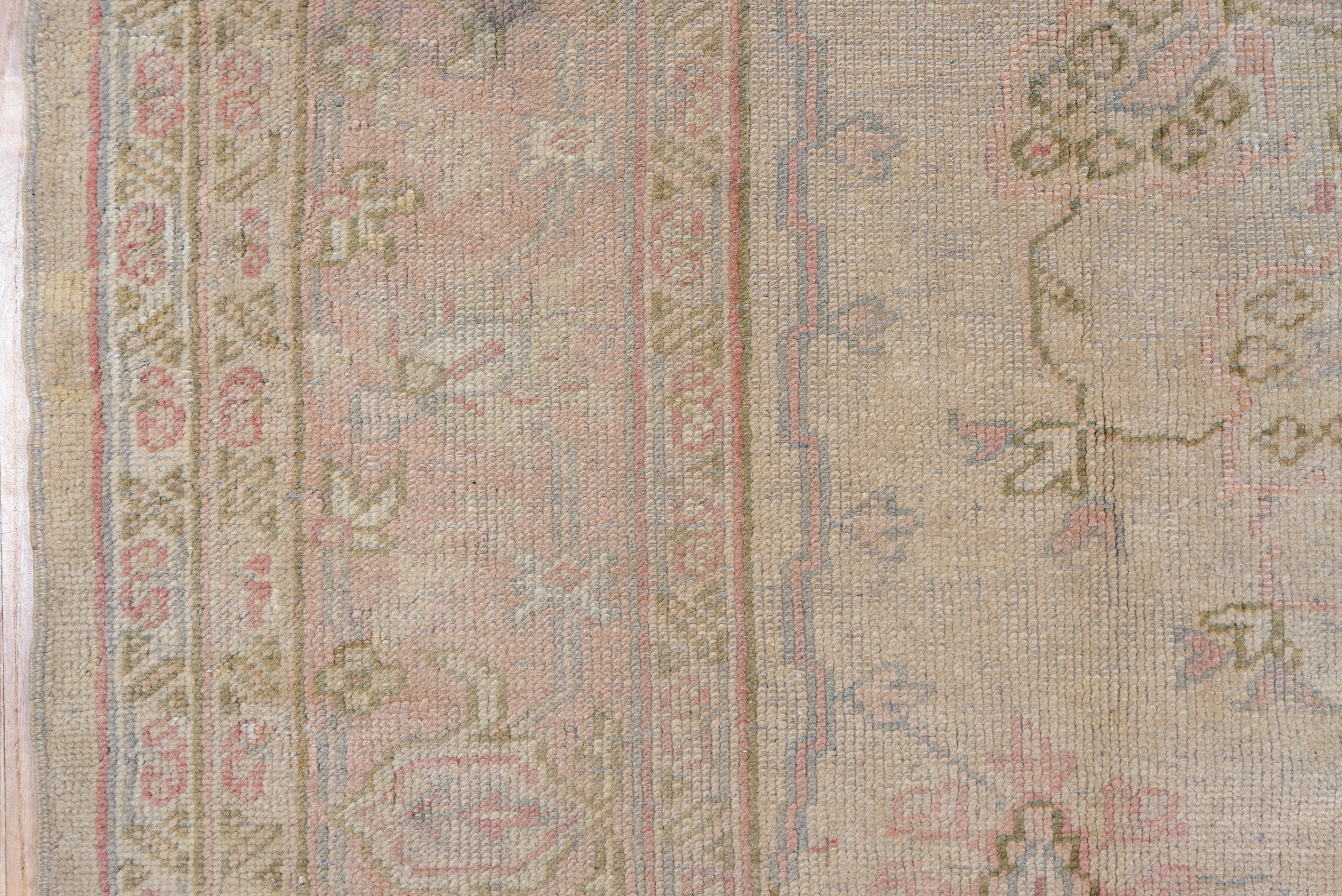 The cream pink sub- field shows an open layout of short floral sprays around an off-white small medallion. Powder border with widely spaced geometric palmettes. Coarse weave, slight all-over pile wear. Generally soft palette.