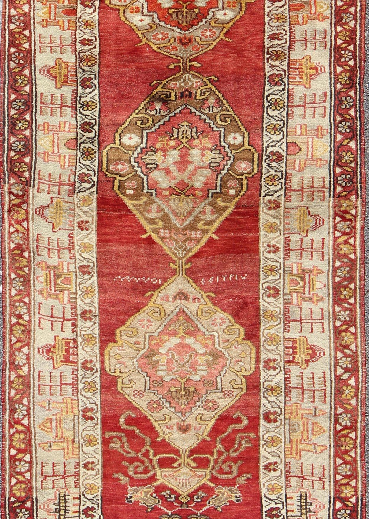This colorful Oushak carpet rests beautifully upon a field of elegant red. A large medallion of brown, taupe, yellow and gray takes center stage and is well balanced by four prominent organic corner motifs composed of various muted taupe and light