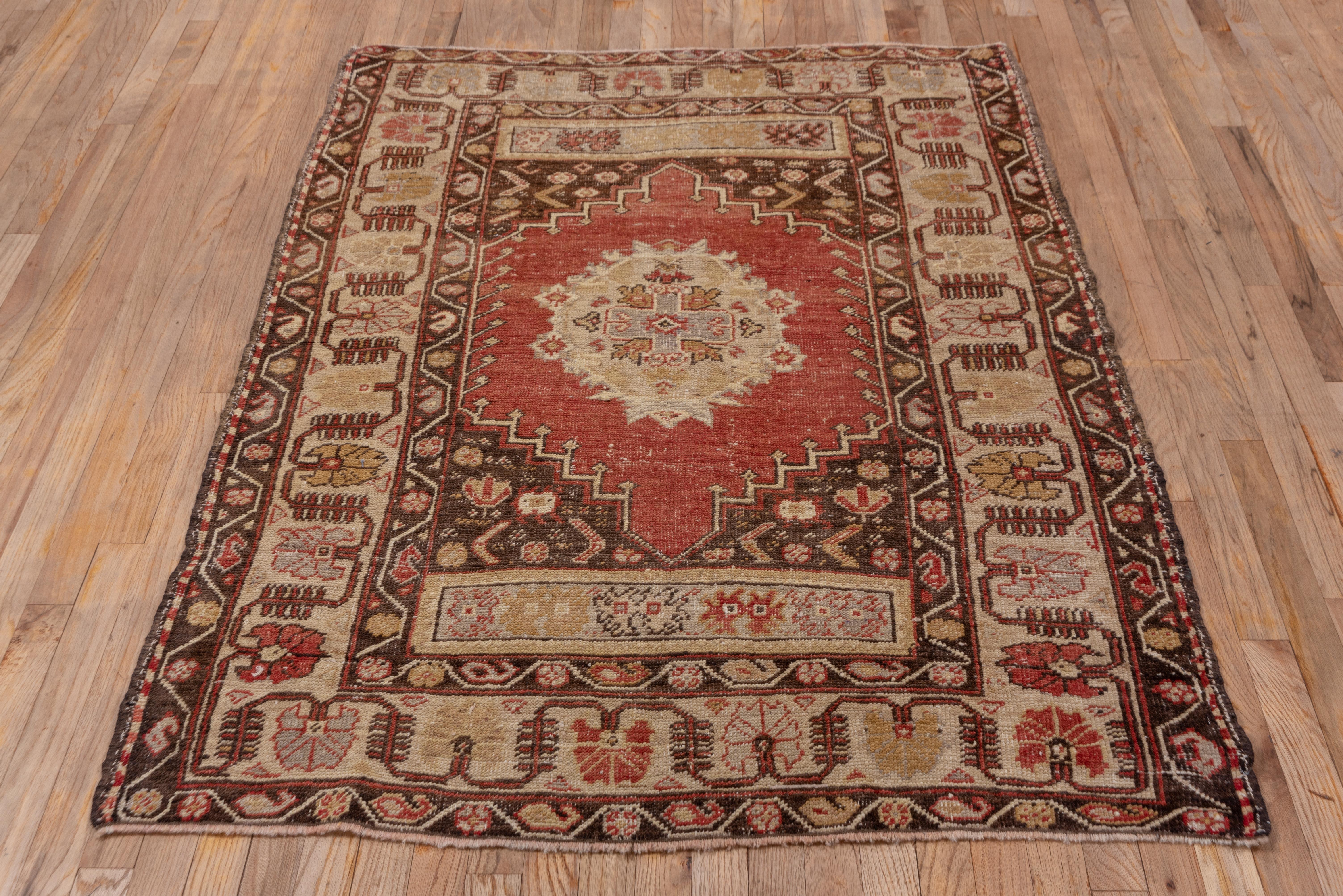 A cream border of reversing large carnations surrounds the red field with a hexagonal medallion and khaki end panels with simple ragged palmette motives. Botehs and rosettes decorate the brown guard stripes of this fair condition Anatolian scatter.