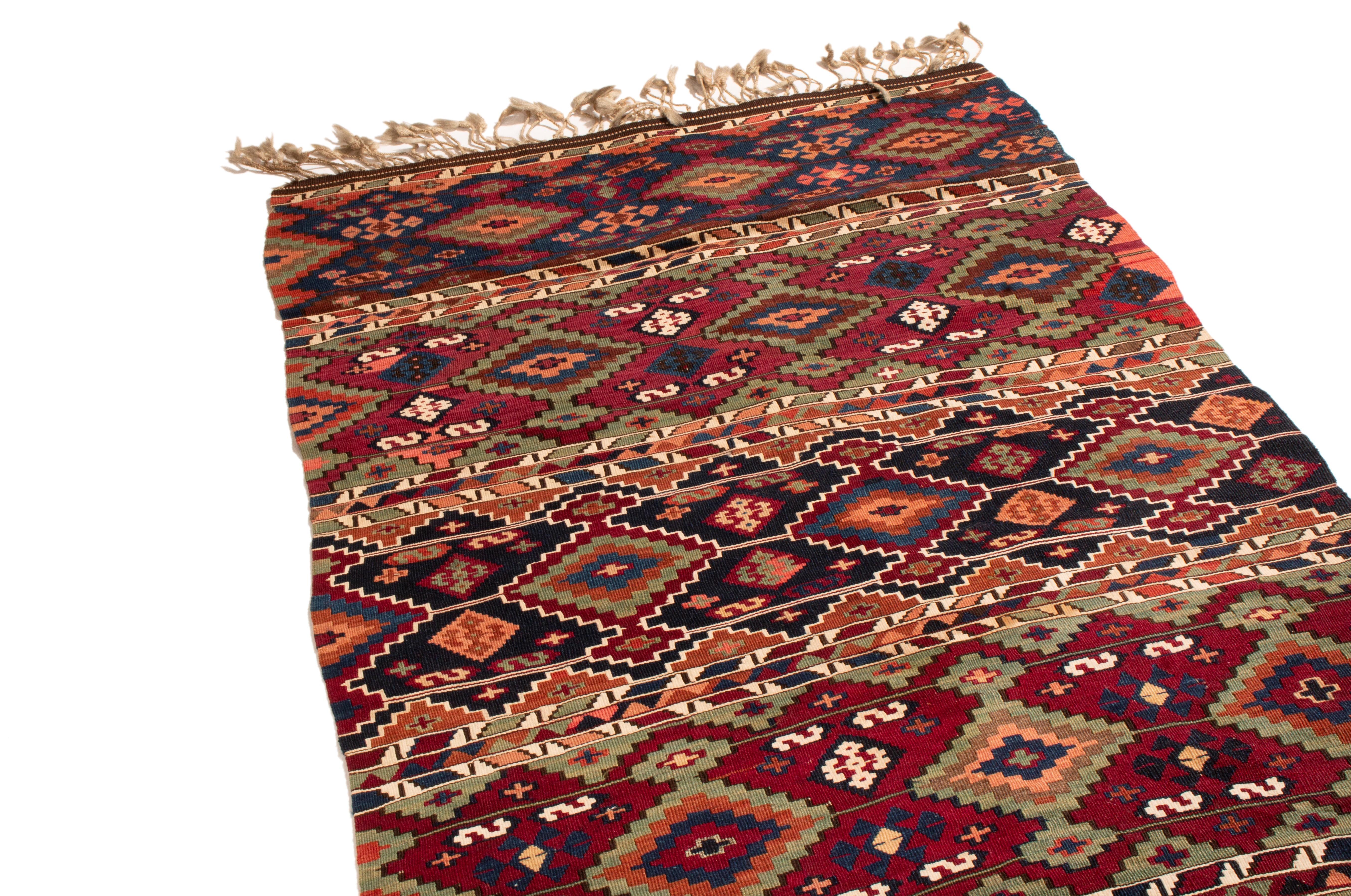 Originating from Turkey between 1900-1920, this antique geometric wool Kilim rug features a distinct combination of both iconic and seldom-seen Turkish symbols. Flat-woven in high-quality wool, the alternating rows of burgundy red and navy blue with