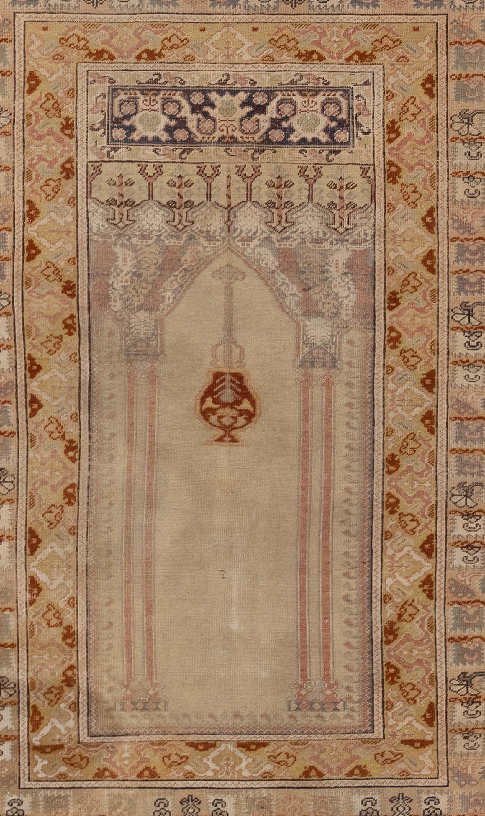 An antique Turkish Kaiseri prayer rug from the 1900s. It features a finely woven silk in the Turkish style with an ecru field. The rug has a scalloped top with a mosque lamp and two ornamental columns supporting a deep spandrel panel. Above and