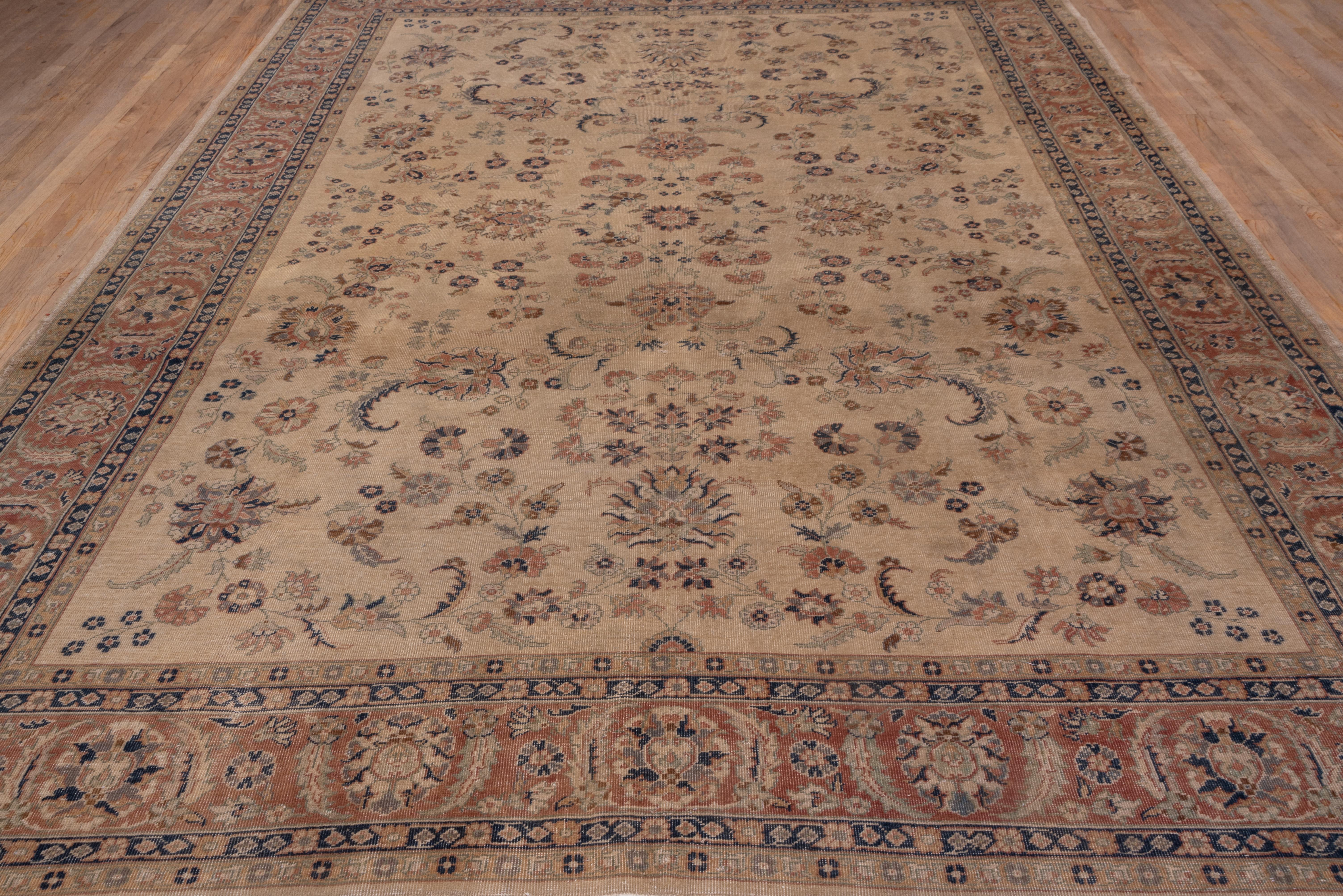 The straw field presents a detached pattern of carnations, ragged palmettes, rosettes and blossoming vine segments, arranged around a central sharply petaled rosette. The medium brown border of this fair condition carpet shows in and out palmettes