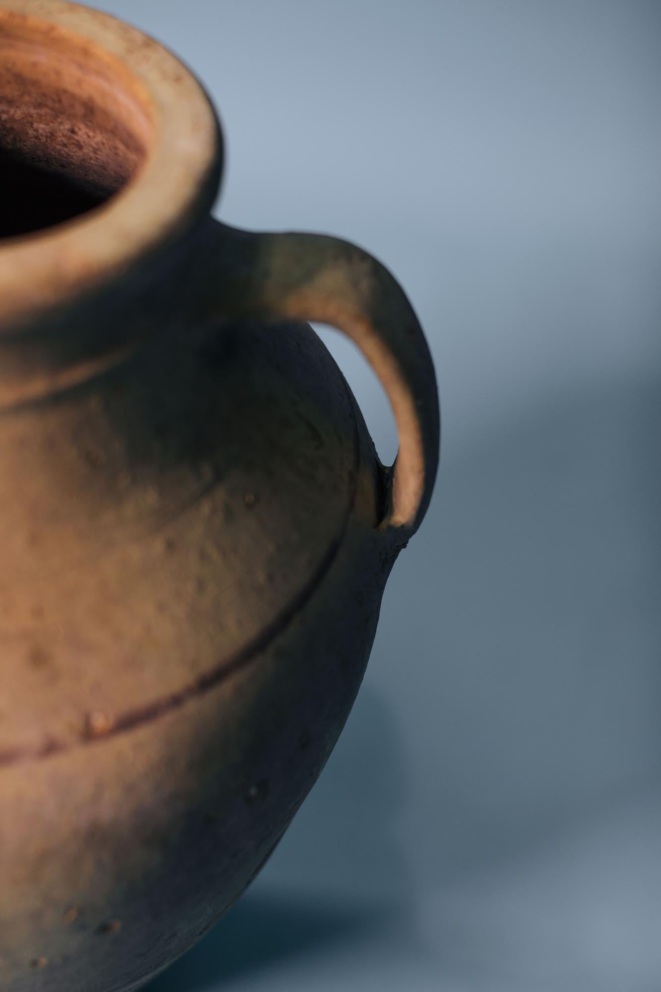 This antique terracotta storage jar embodies the quiet beauty and utility of early 20th-century Anatolian craftsmanship. Hand-thrown in rural Turkey, its tall, tapered silhouette and twin handles were designed for everyday use — most commonly for