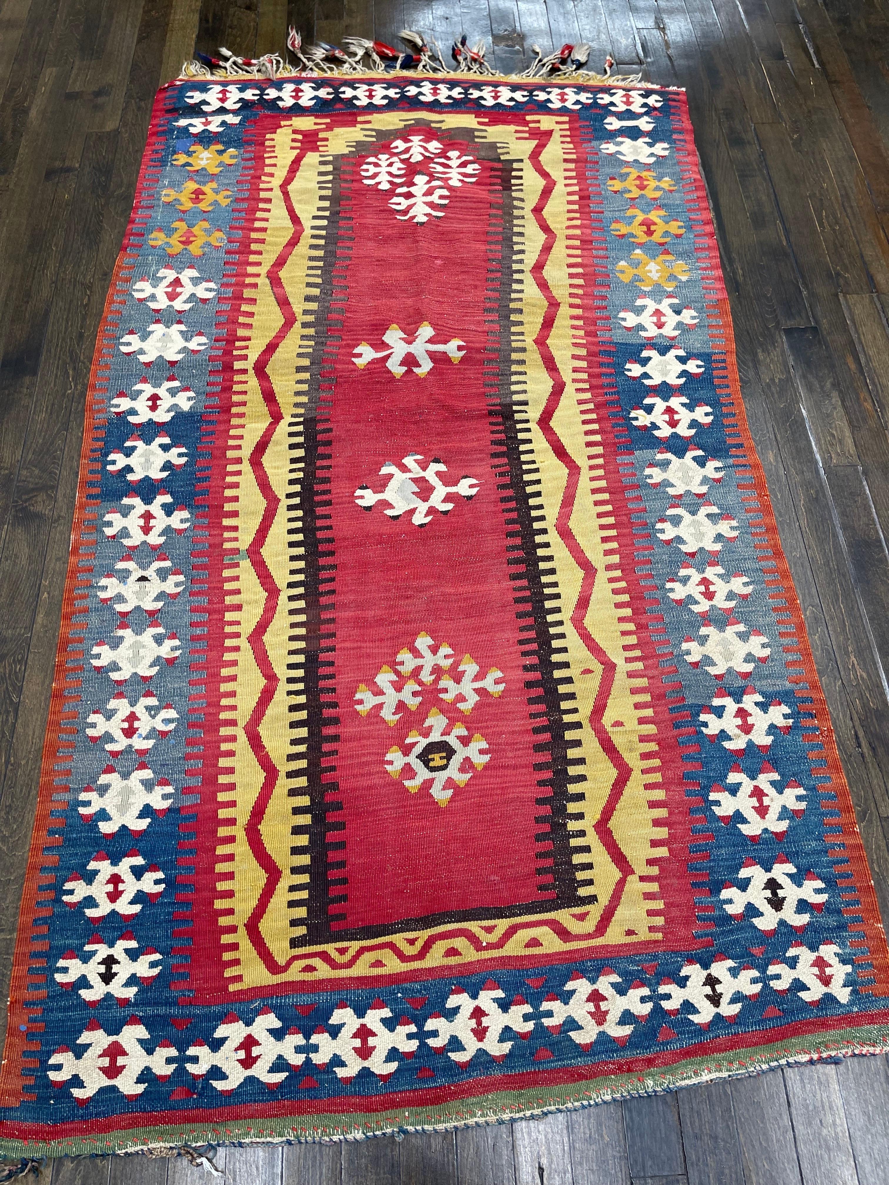 Attributed to Yoruk, this flat weave kilim features a tomato red panel in the middle decorated with scattered ivory rossetts framed with a very bright yellow with abstract red lines moving around it.The whole kilim is then surrounded with a