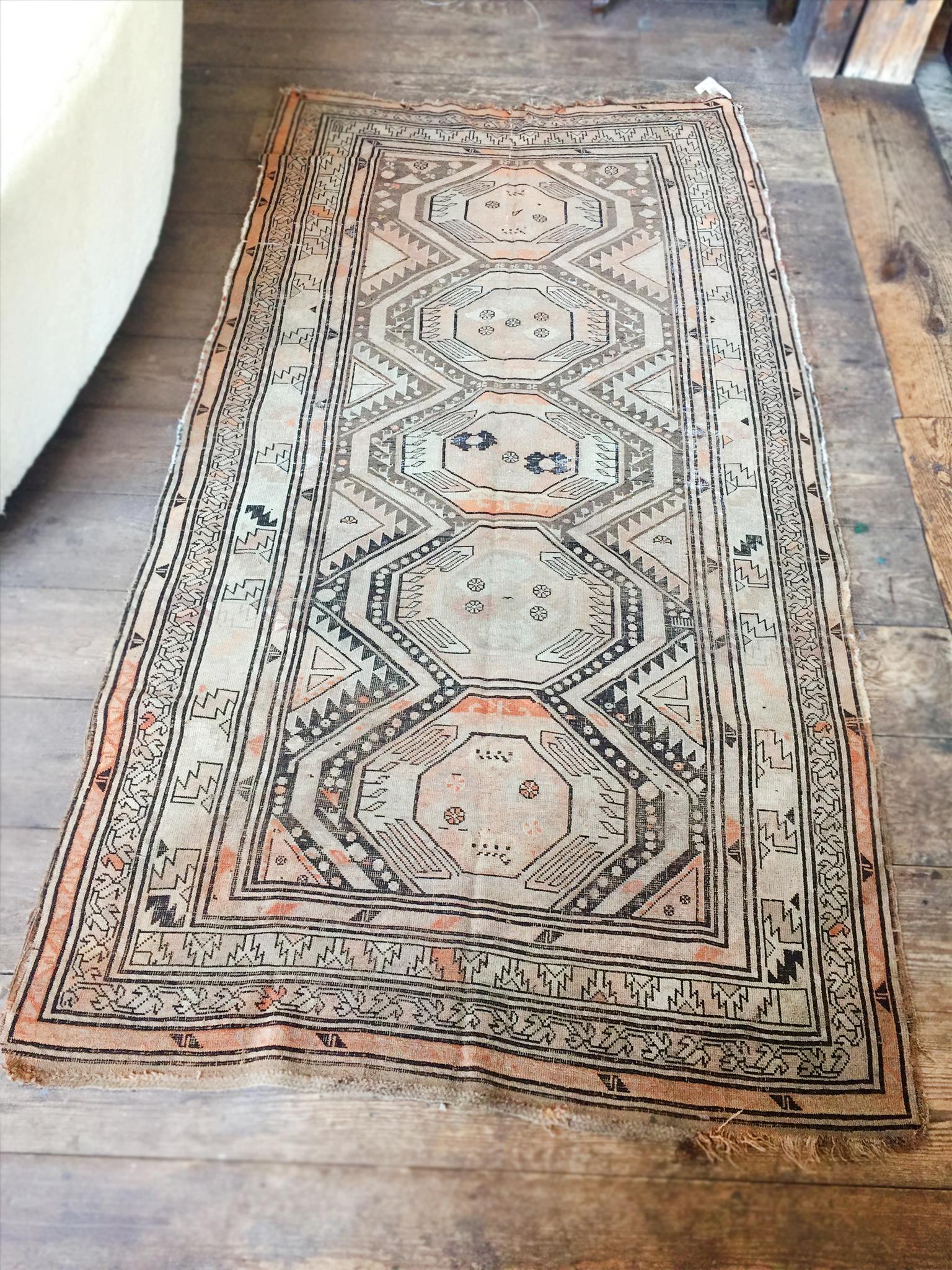 This antique Turkoman runner rug was handwoven in the late 19th-early 20th century. It is comprised of hand-dyed wool, with a palette of brown, tan, ivory, and hints of orange. The main design is a bold series of geometric medallions that run
