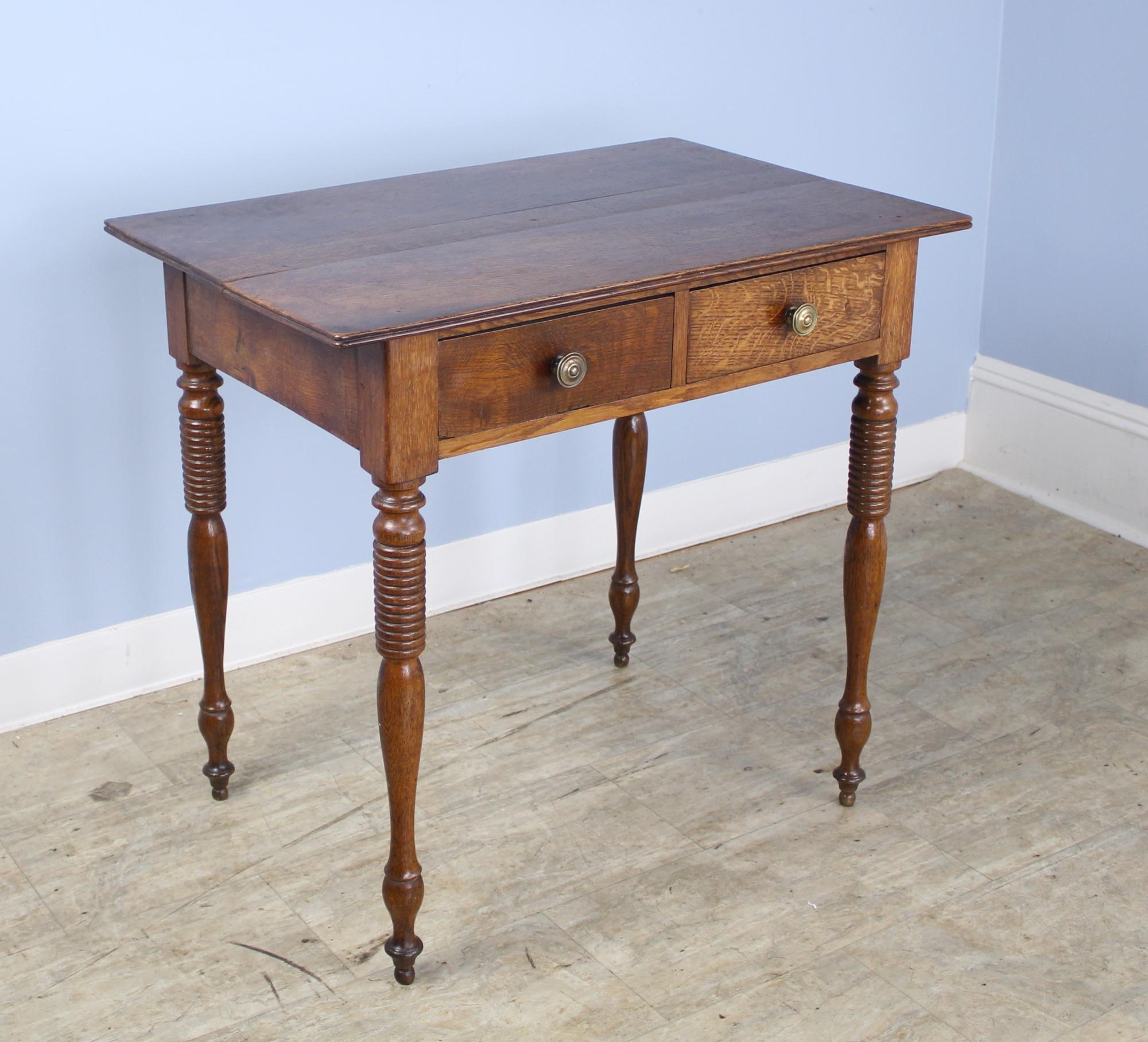 A charming French oak side table with two clean drawers and eye-catching turned legs. The top is in good condition and is accented with a reeded edge. Small ball feet complete the look.