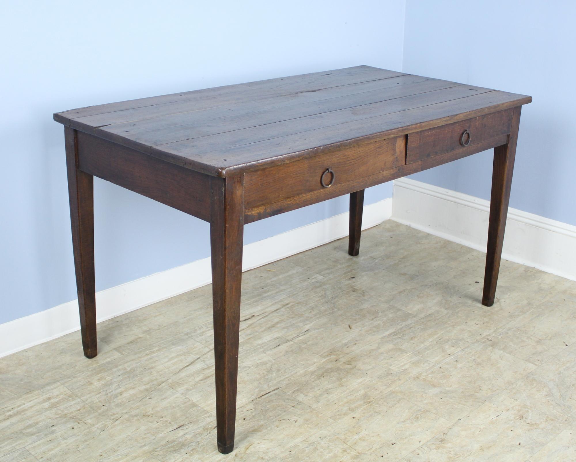 A handsome rustic oak writing table, generously proportioned with two front drawers. Classic tapered legs and good dark oak color. 24 inch apron height is allows for good knee room.