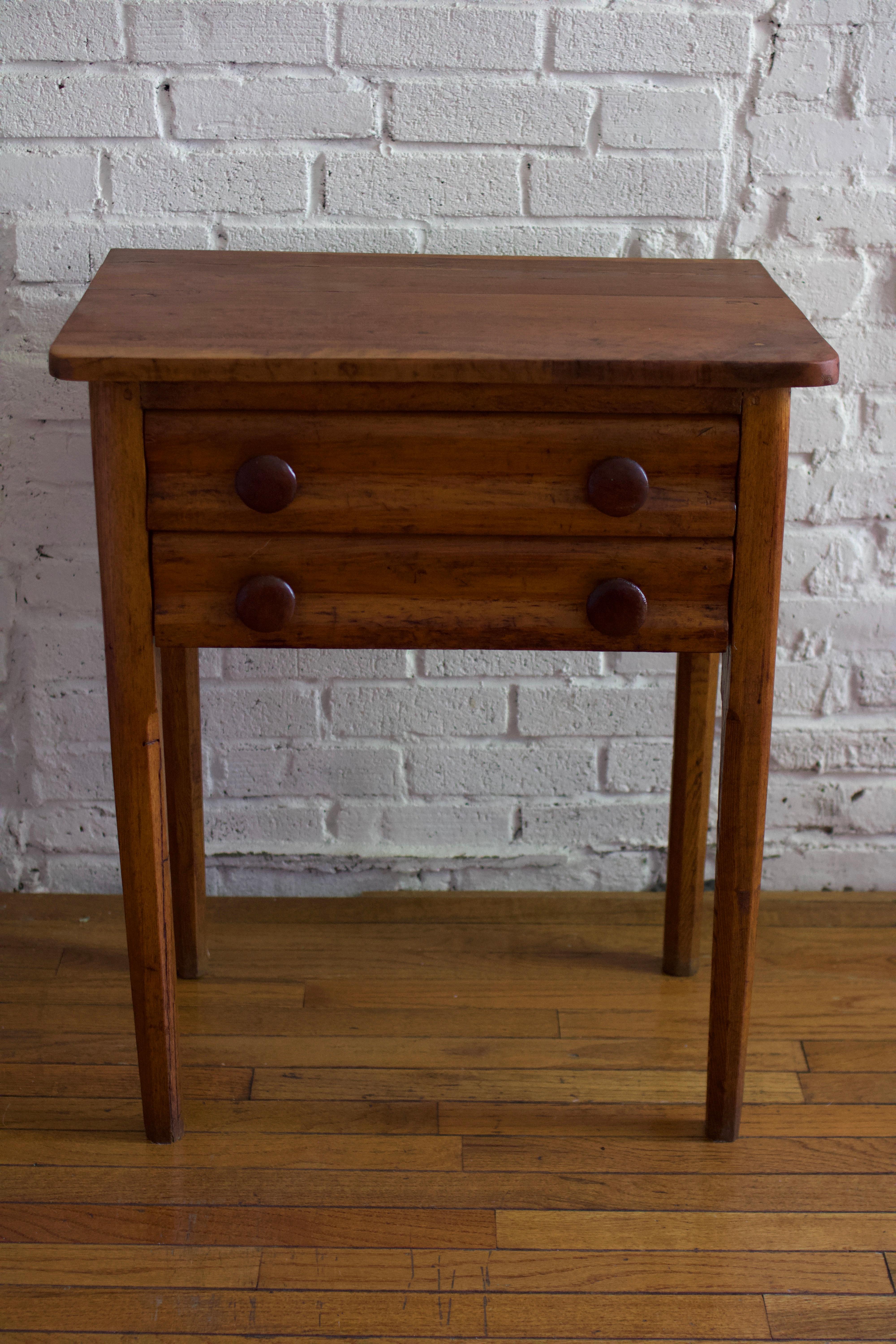Unique mid to late 19th century stand / end table. This primitive meets Americana style table features two drawers with a bow-front roll design, solid-wood knobs and tapered legs. The dovetail drawers are in solid condition. The rectangle top