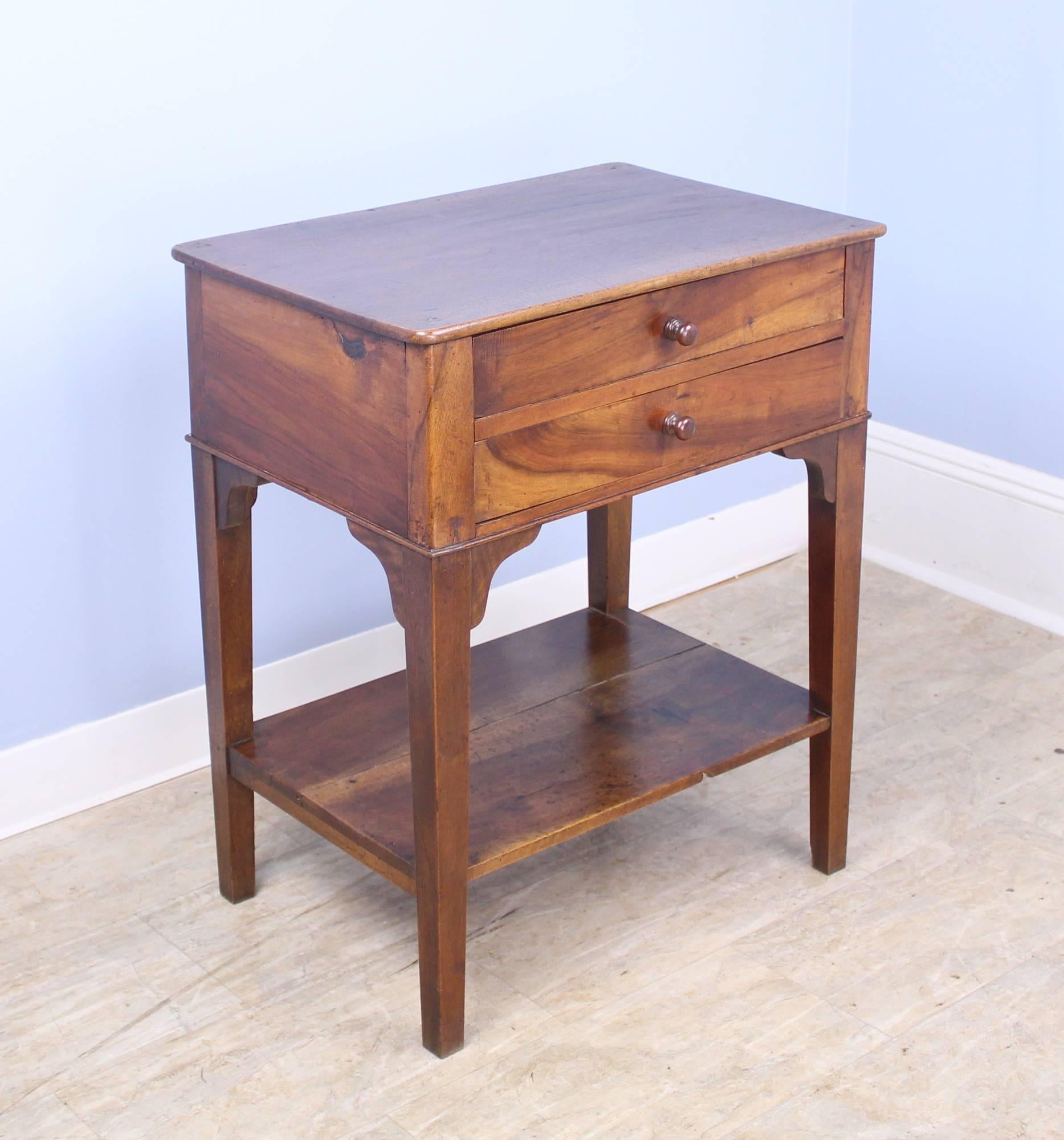 A highly functional two-drawer walnut side table with lower shelf. Beautiful walnut grain and lovely patina. Would make a nice lamp or occasional table, or a single nightstand.