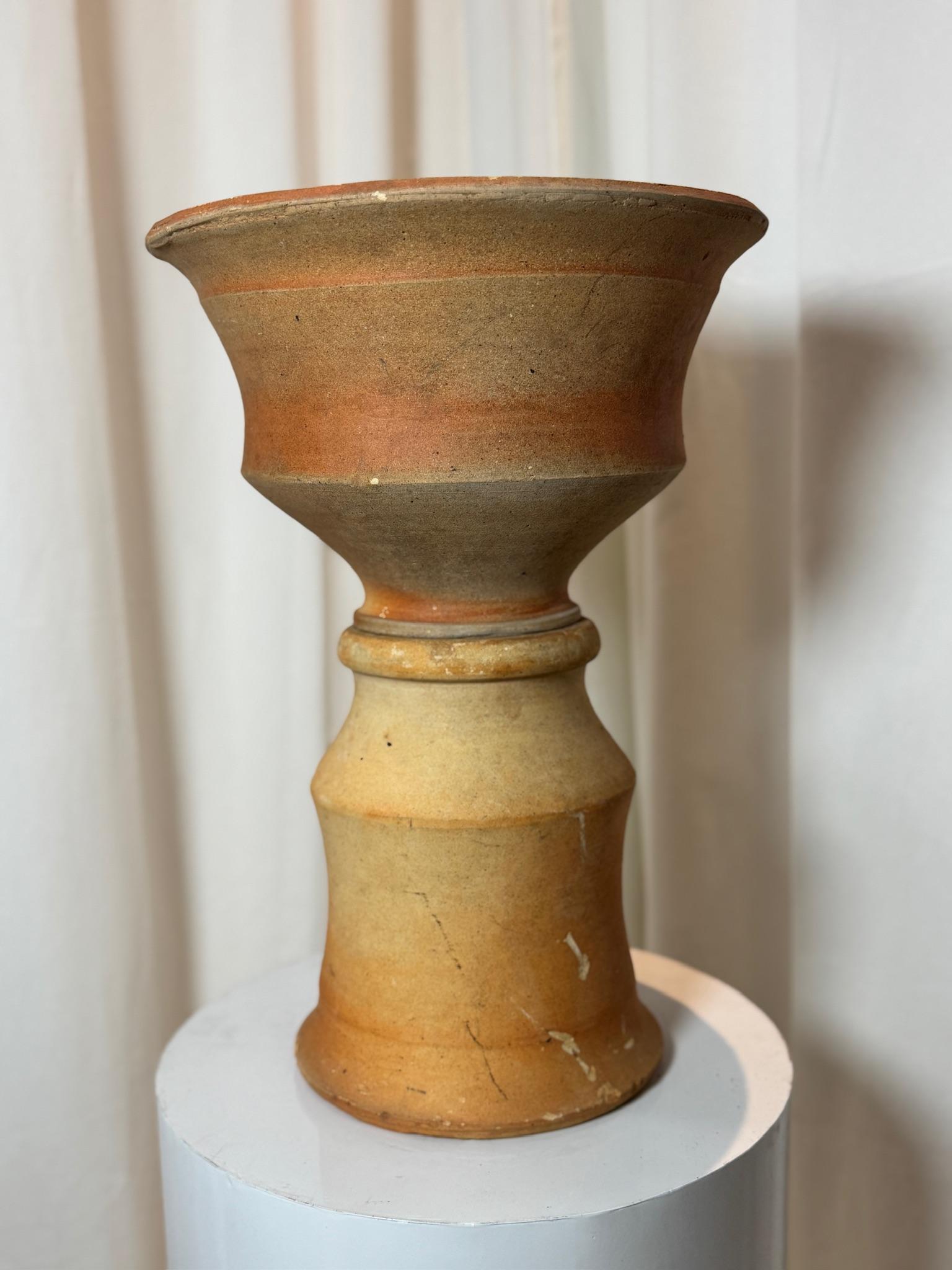 Questo antico vaso in terracotta in due pezzi è un notevole esempio di ceramica artigianale, con una forma ispirata alla clessidra che emana un fascino rustico e scultoreo. Il vaso è composto da due pezzi separati e impilabili, che si incastrano