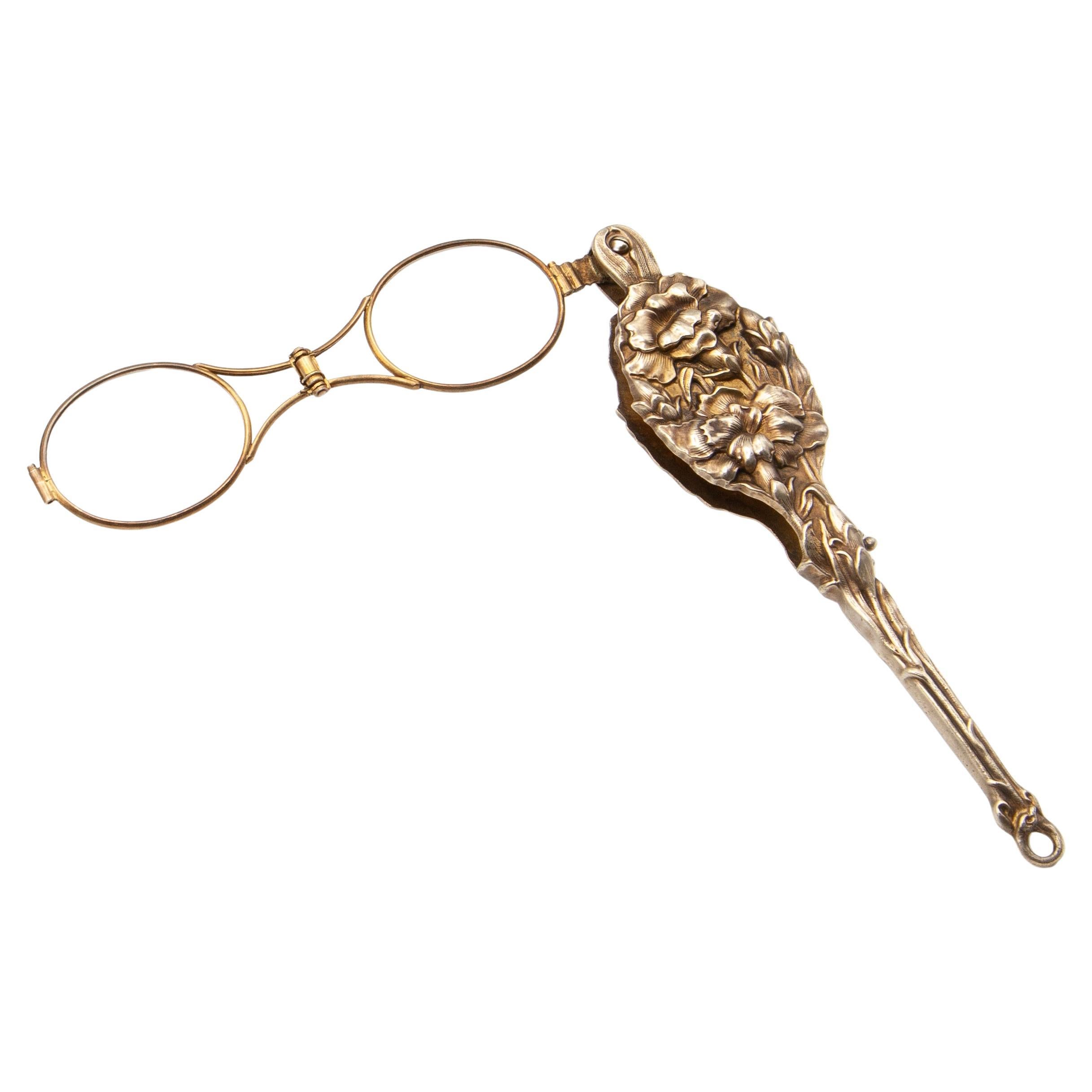 An exquisite antique Art Nouveau lorgnette, circa 1900s by Unger Brothers, featuring a silver vermeil repoussé handle and case richly decorated with high-relief floral motifs. The elegant spring-loaded mechanism reveals a pair of folding spectacles