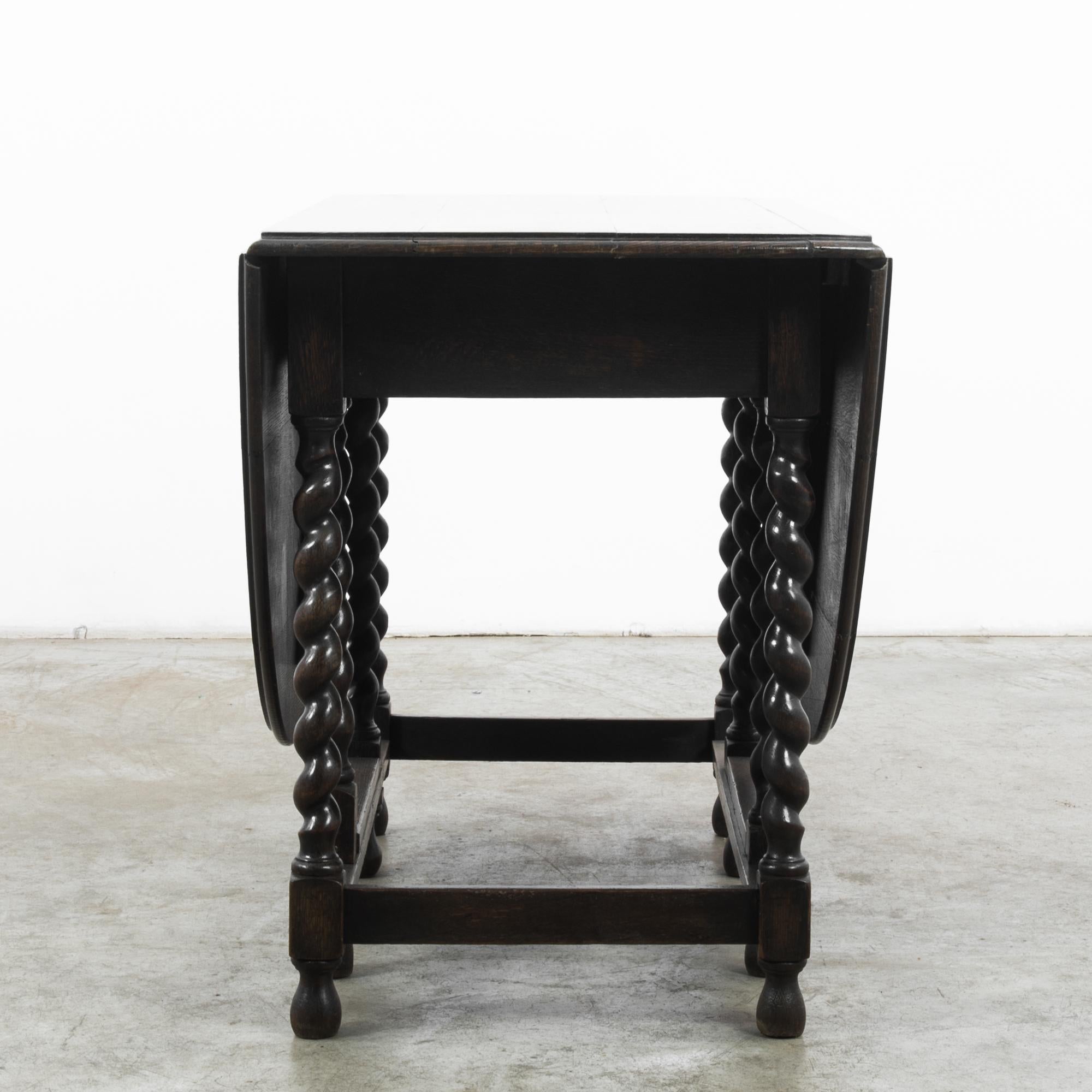 This antique gateleg table was made in the United Kingdom. The striking barley twist legs give it a stately, old-world charm. It features a rich, deep tone, polished to highlight the elegant wood swirls on the tabletop. The sides of the circular