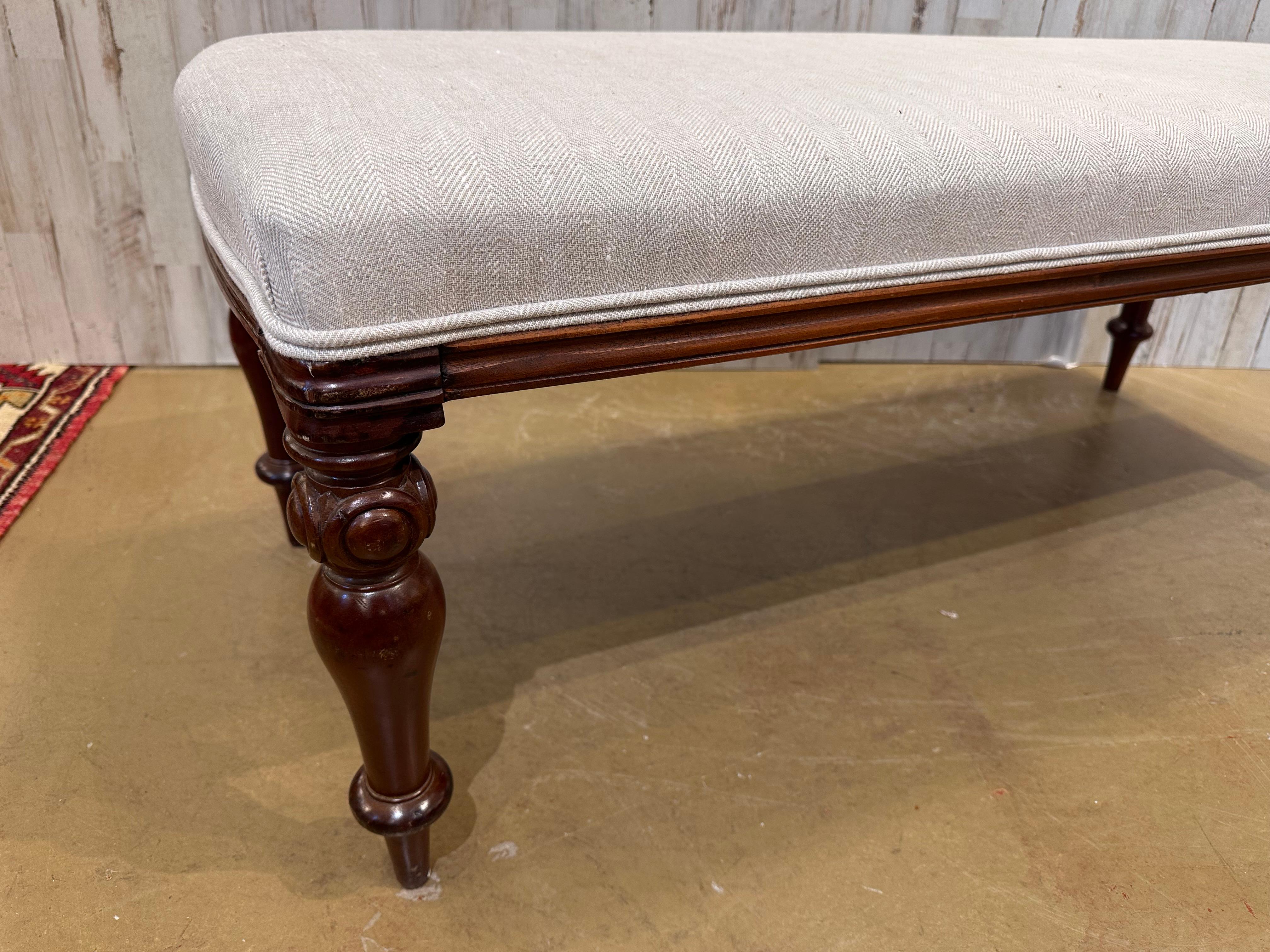 This is a beautiful antique English bench! Newly reupholstered, this bench is in stunning condition. The legs are sturdy and firm, with a lovely patina and hand carved detailing as well as turned design. The new fabric is a neutral cream that would