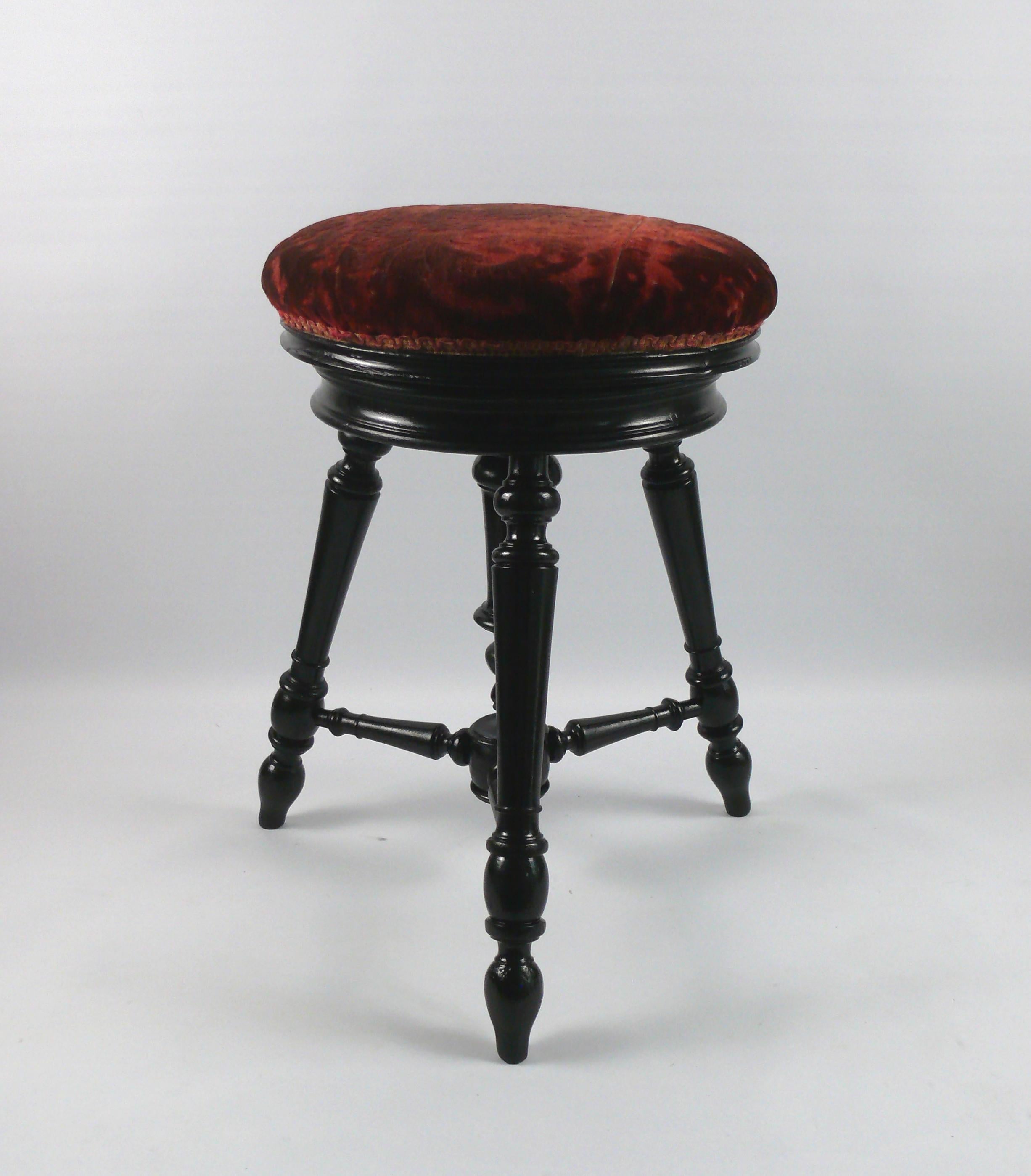 Antique piano stool from France, around 1880. The piano stool has a frame made of 3 slanted, turned legs which carry the plate with the spindle nut. The legs are held together at the bottom by decorative struts. The steel spindle is covered by a