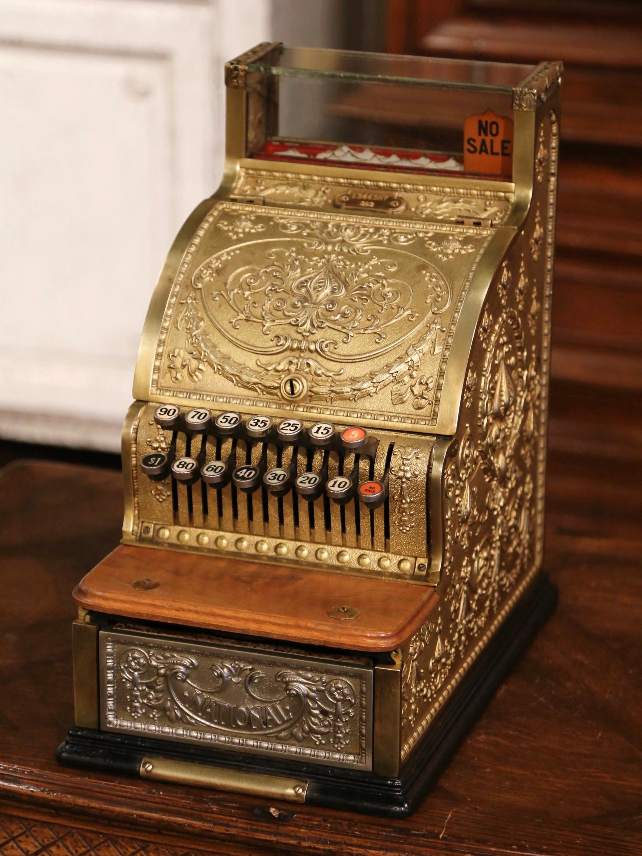 This antique cash register was built circa 1915, made in nickel, brass, and wood and embellished with ornate designs picturing ribbons, acanthus leaves, and other designs. The number plaques at the top of the machine which correlate to the bright