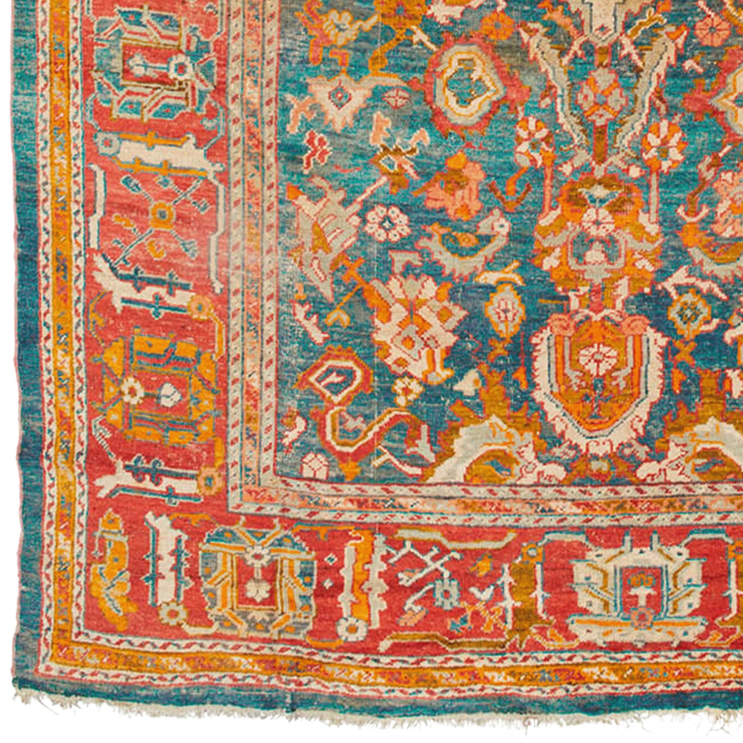 Un antico tappeto Ushak anatolico, seconda metà del XIX secolo. Ca 432-434 x 317,5-331,5 cm.

Un fondo blu con un grande motivo policromo di fiori stilizzati, bande di nuvole, palmette, ornamenti floreali e medaglioni. Un ampio bordo principale