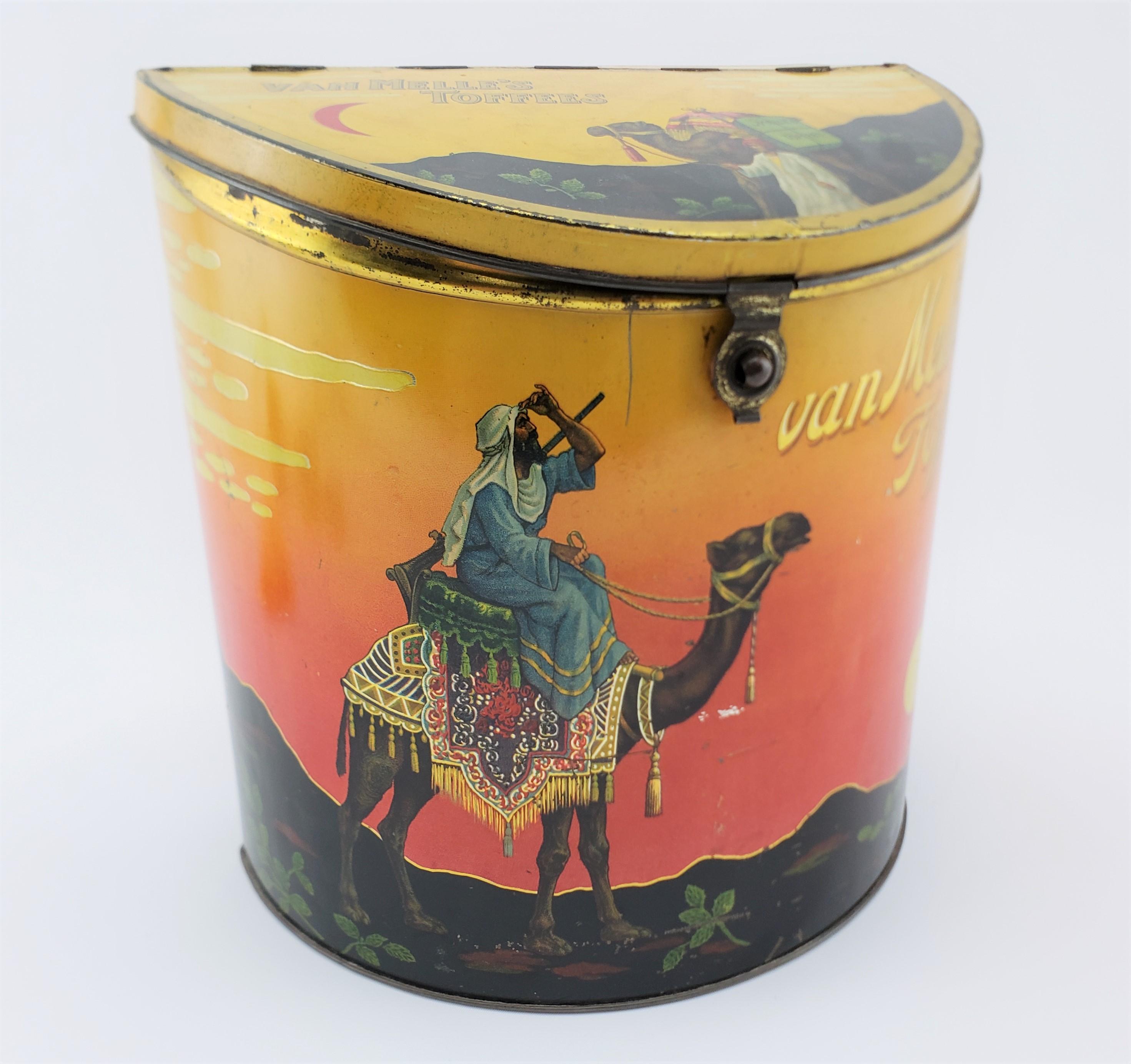 This antique Van Melles store display tin was made in Amsterdam in approximately 1925 in the period Art Deco style. The tin is half moon shaped with a hinged lid with a fold over clasp on the front. The entire tin is decorated with a desert vignette