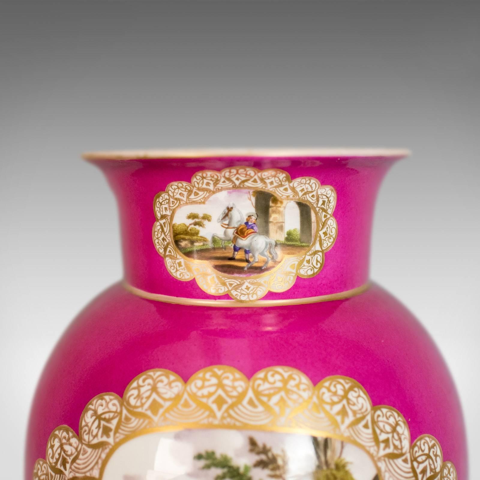 This is an antique vase, a German porcelain flower vase monogrammed 'AR' beneath and dating to the late 19th century.

A large piece in very good order throughout
Painted scenes on a vivid cerise ground
Highlighted with golden trace to the neck