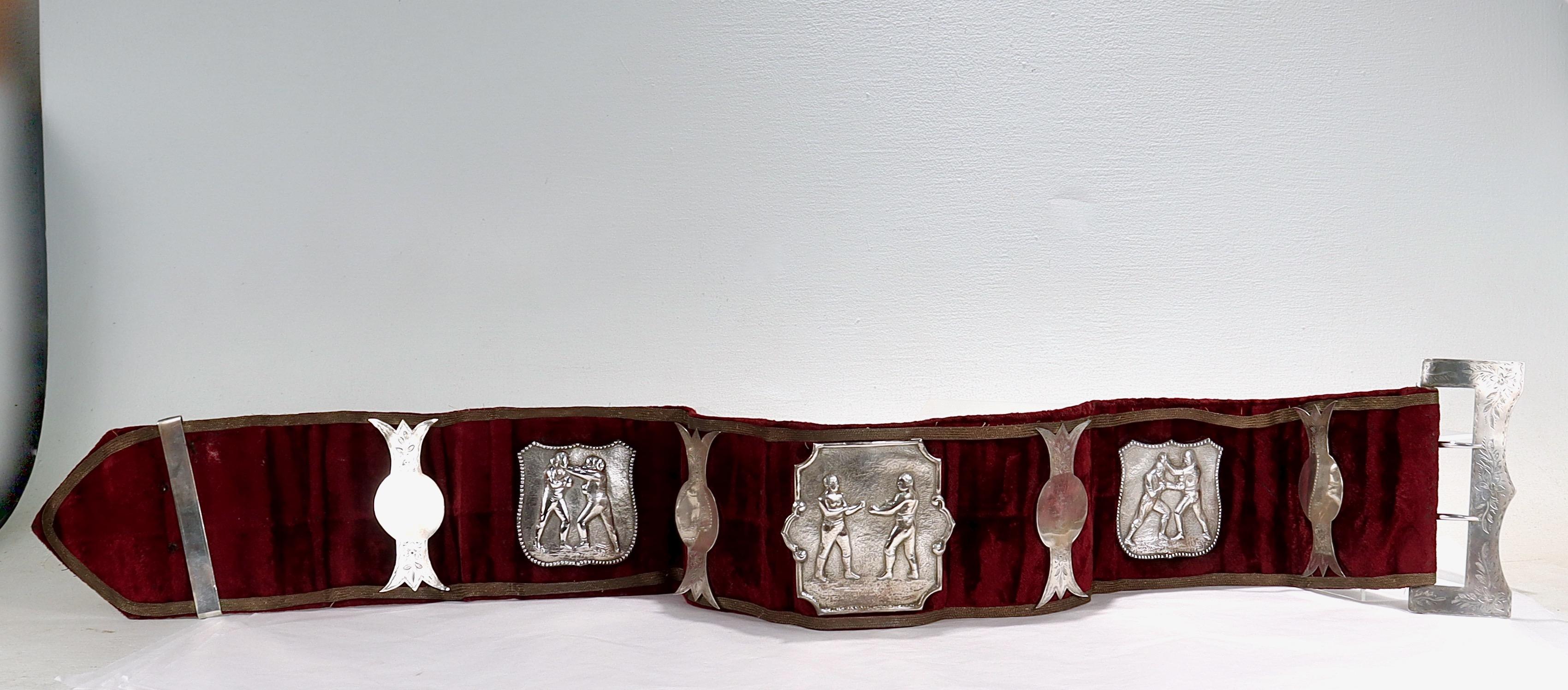 A fine antique boxing champion's belt.

The belt consists of a wide velvet belt with piping stitched around its borders, a solid silver buckle and opposing c-shaped brake, etched silver elements, and 3 repousse medallions of plaques.

Each
