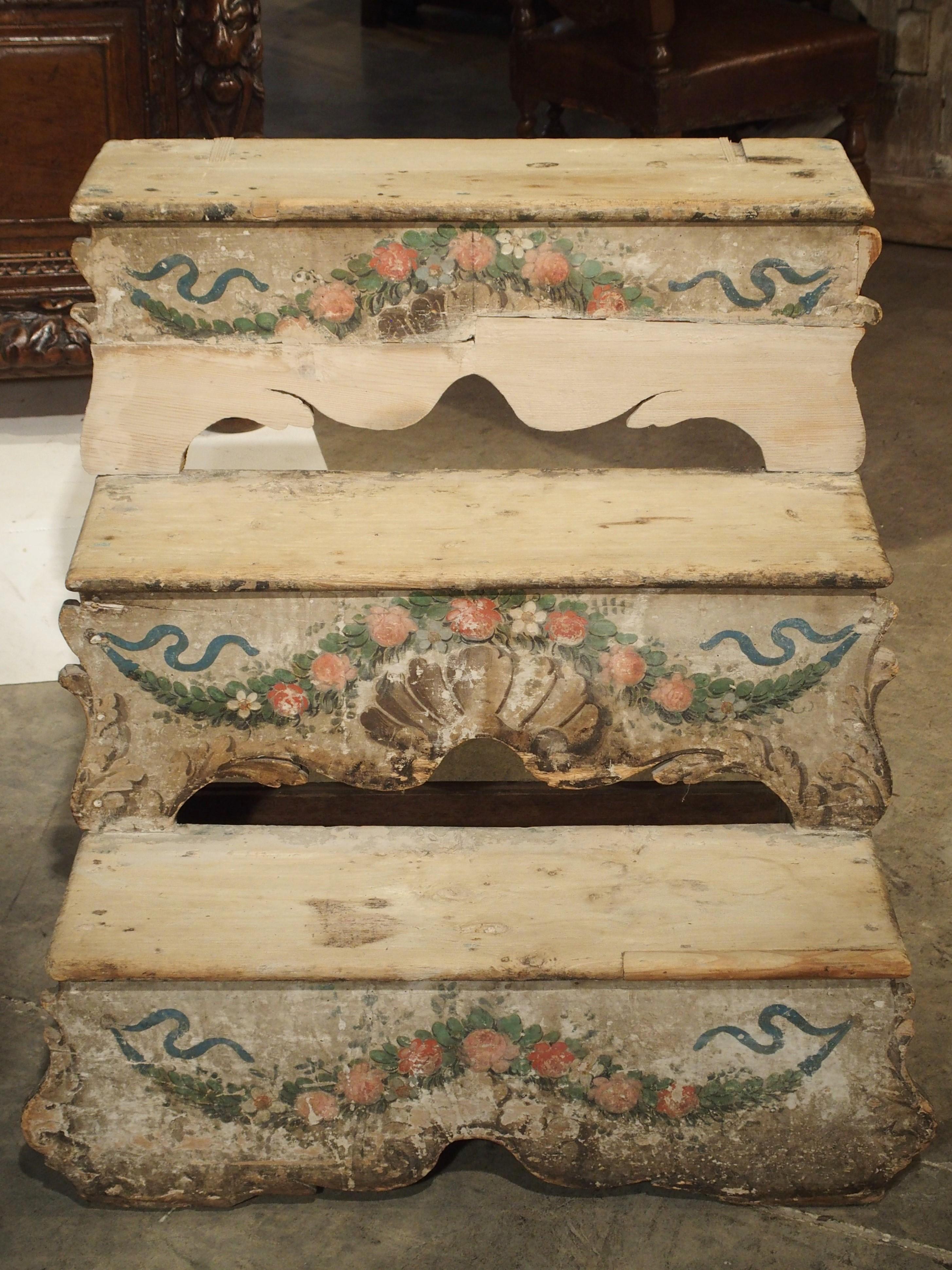 This charming set of stairs is composed of three hand painted steps each measuring roughly 9 3/4 inches high. The motifs on the front of the stairs are swags of pink flowers, acanthus leaves, stylized shells and blue ribbons. On the sides are