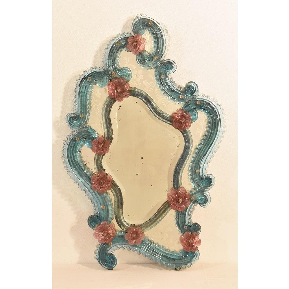 The Antique rectangular venetian mirror  proposed here a rich mirror of volutes and
with a colored glass frame with flowers from the early 20th century. Italian origin. Murano.

The central mirror is beveled and is surrounded by many side mirrors